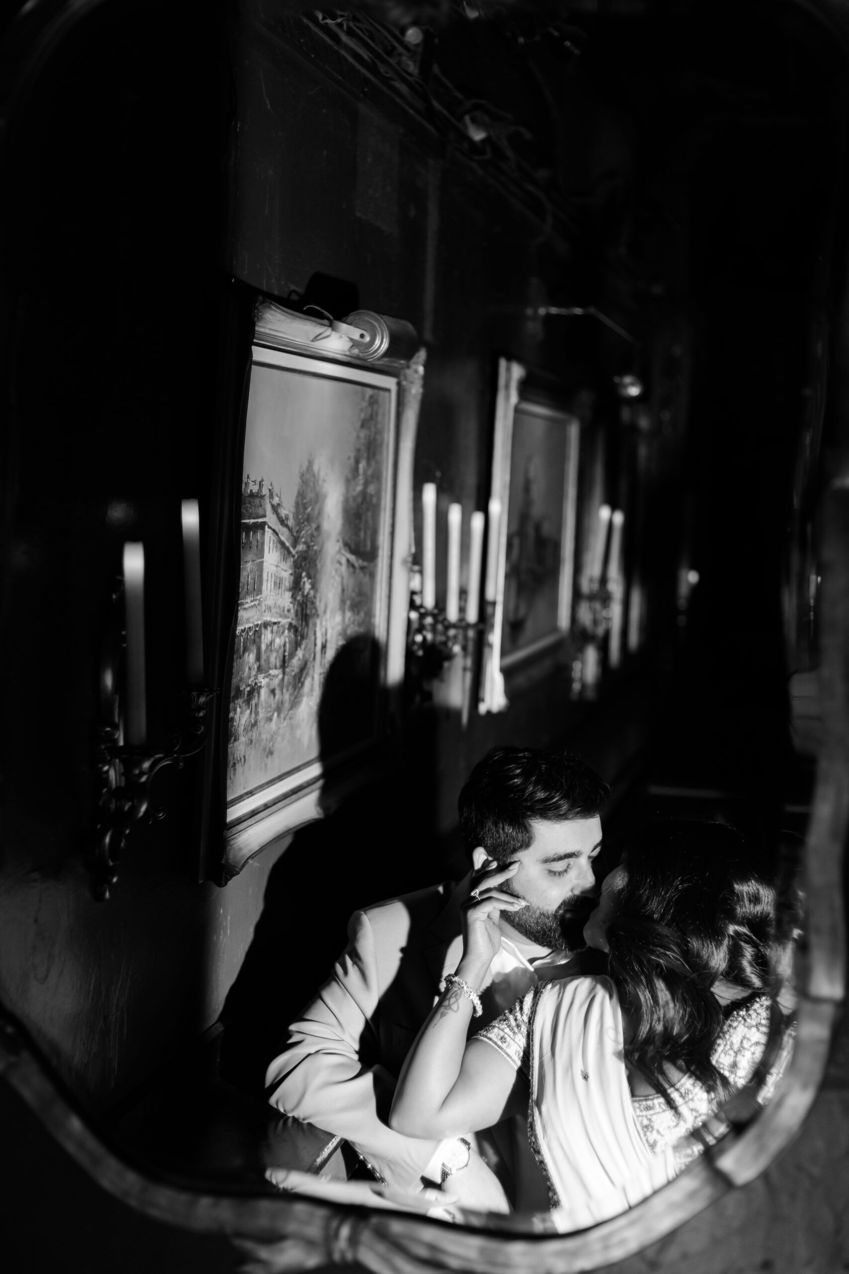 Romantic black and white engagement photo of a couple embracing inside Green Lady Lounge in Kansas City, reflected in a vintage mirror with dramatic candlelight and moody shadows.