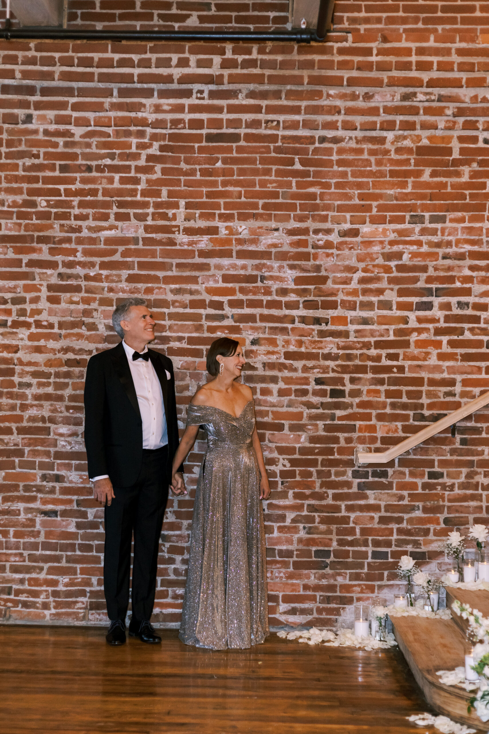 Well-dressed couple holding hands and waiting near a brick wall before the ceremony.