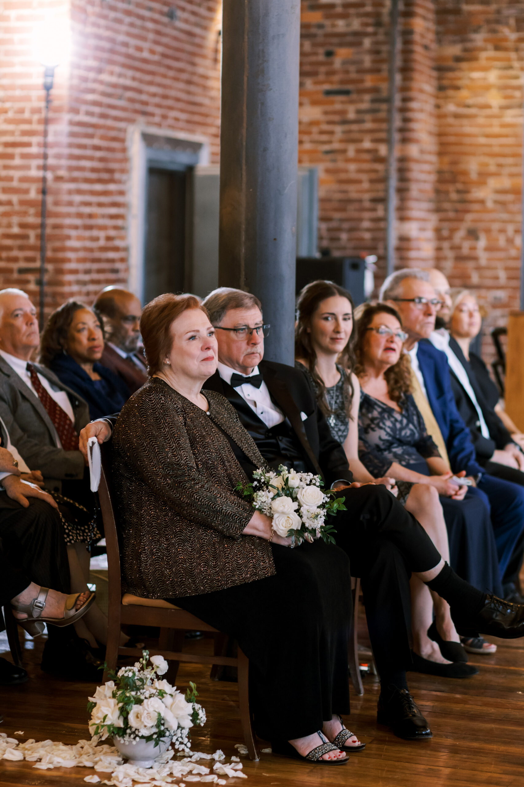 Wedding guests seated in wooden chairs watching the ceremony inside a brick loft space.