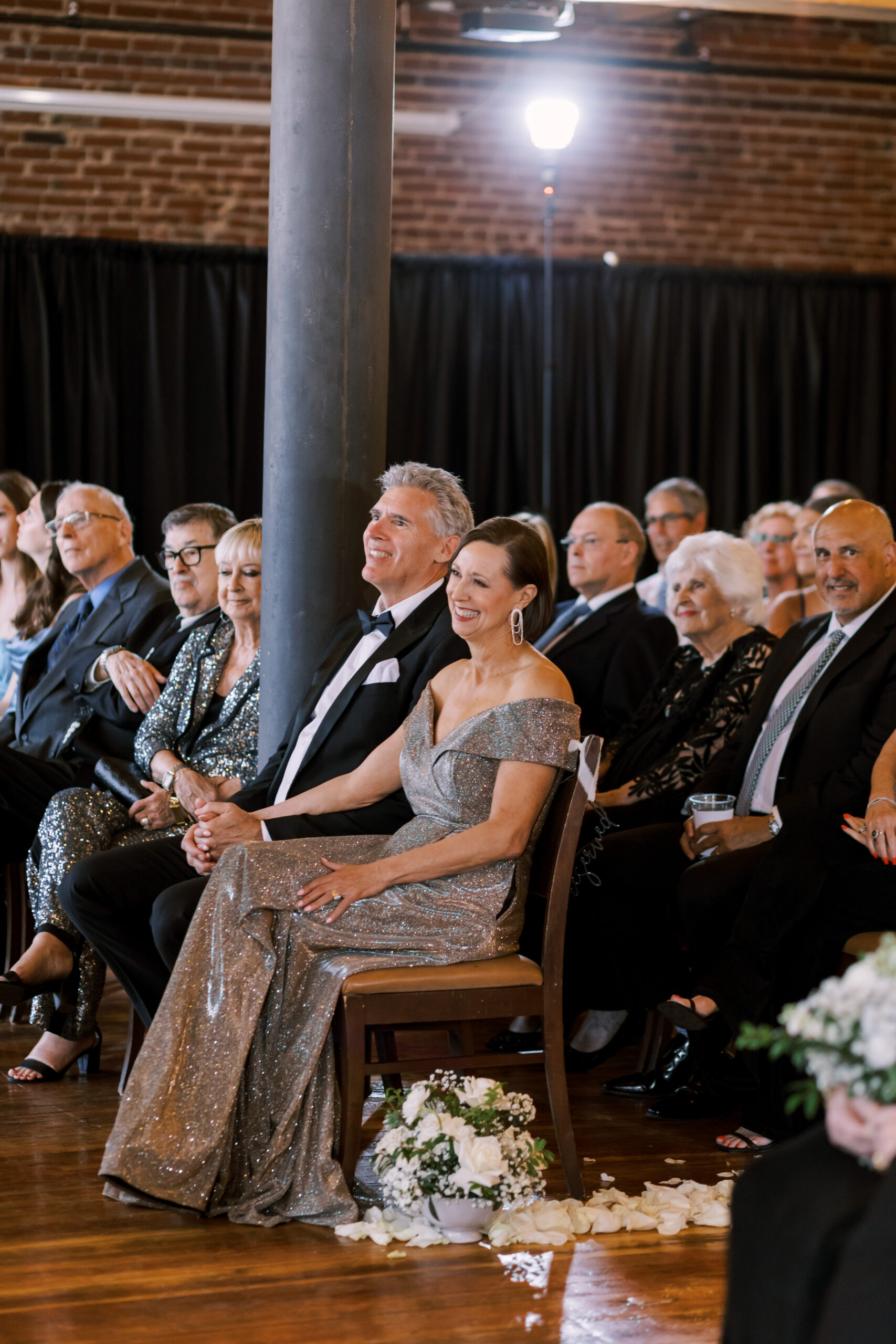 Well-dressed couple seated together smiling while watching the wedding ceremony.