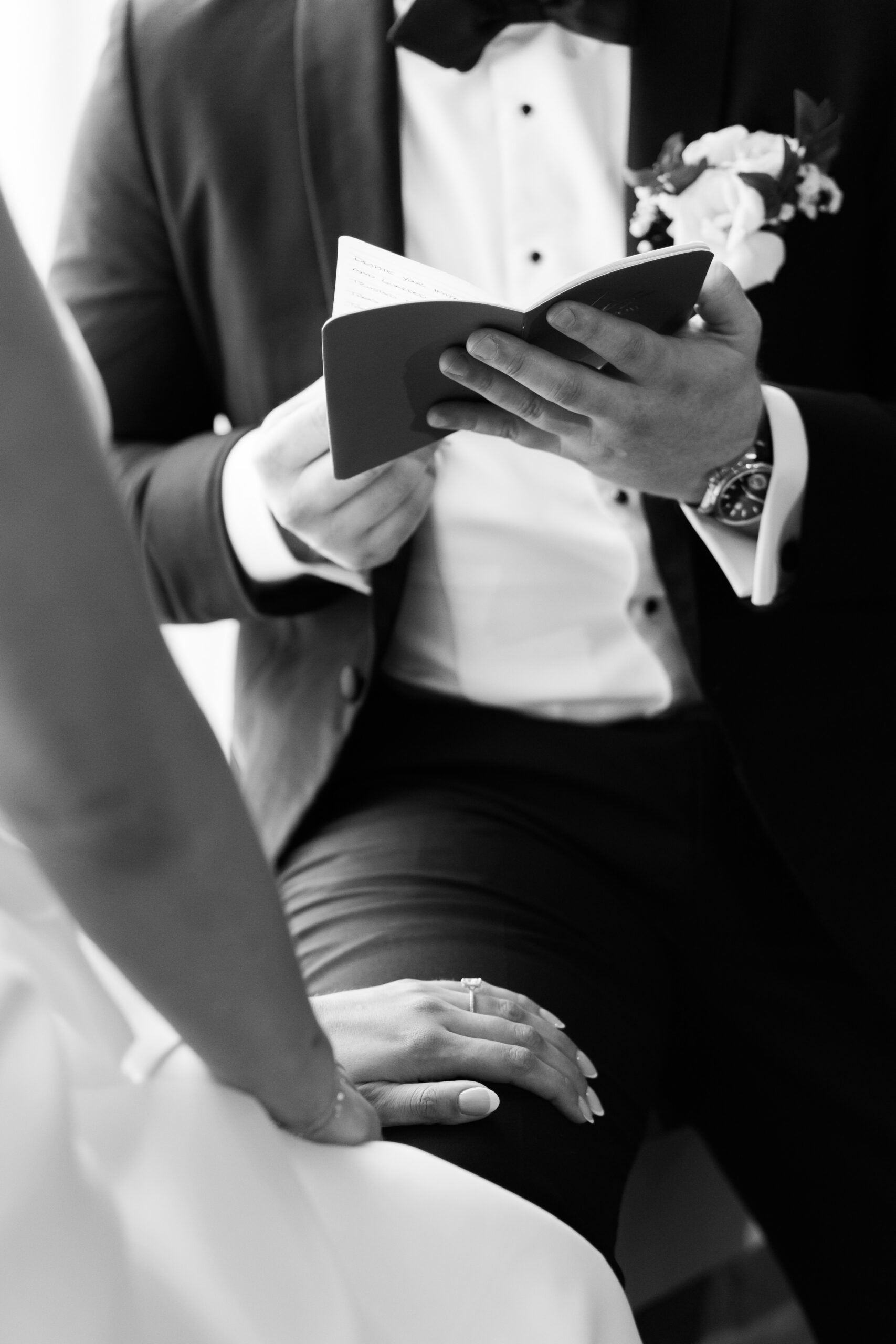 Close-up of the groom holding a small vow book while reading during the ceremony.