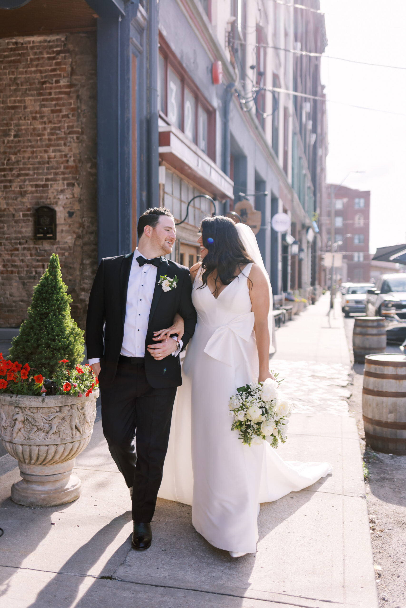 Bride and groom walking arm in arm along a sunny downtown street after the ceremony.