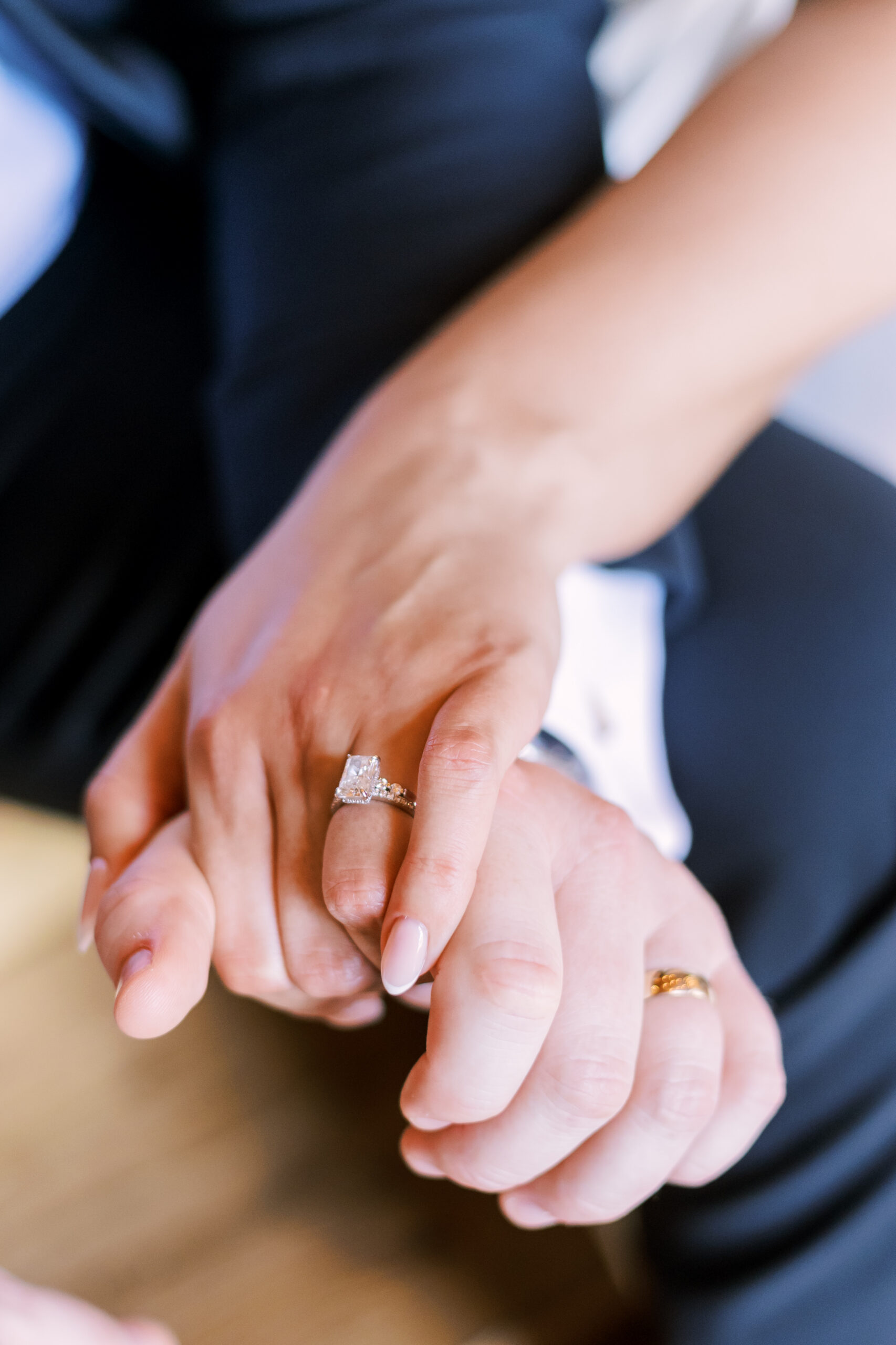 Close-up of bride’s engagement ring and wedding band resting on the groom’s hand.