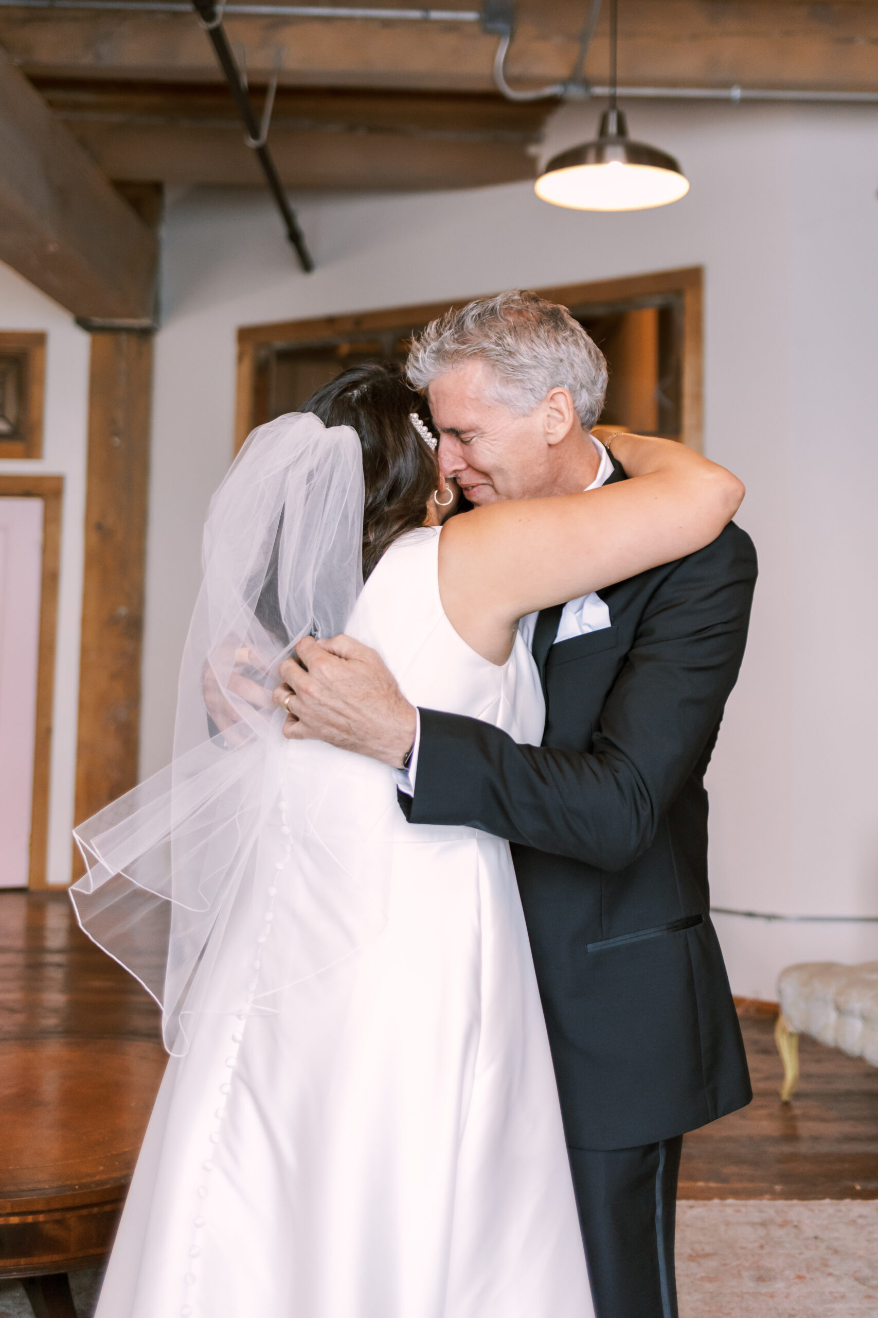 Bride in a veil hugging her father during a quiet moment before the ceremony.