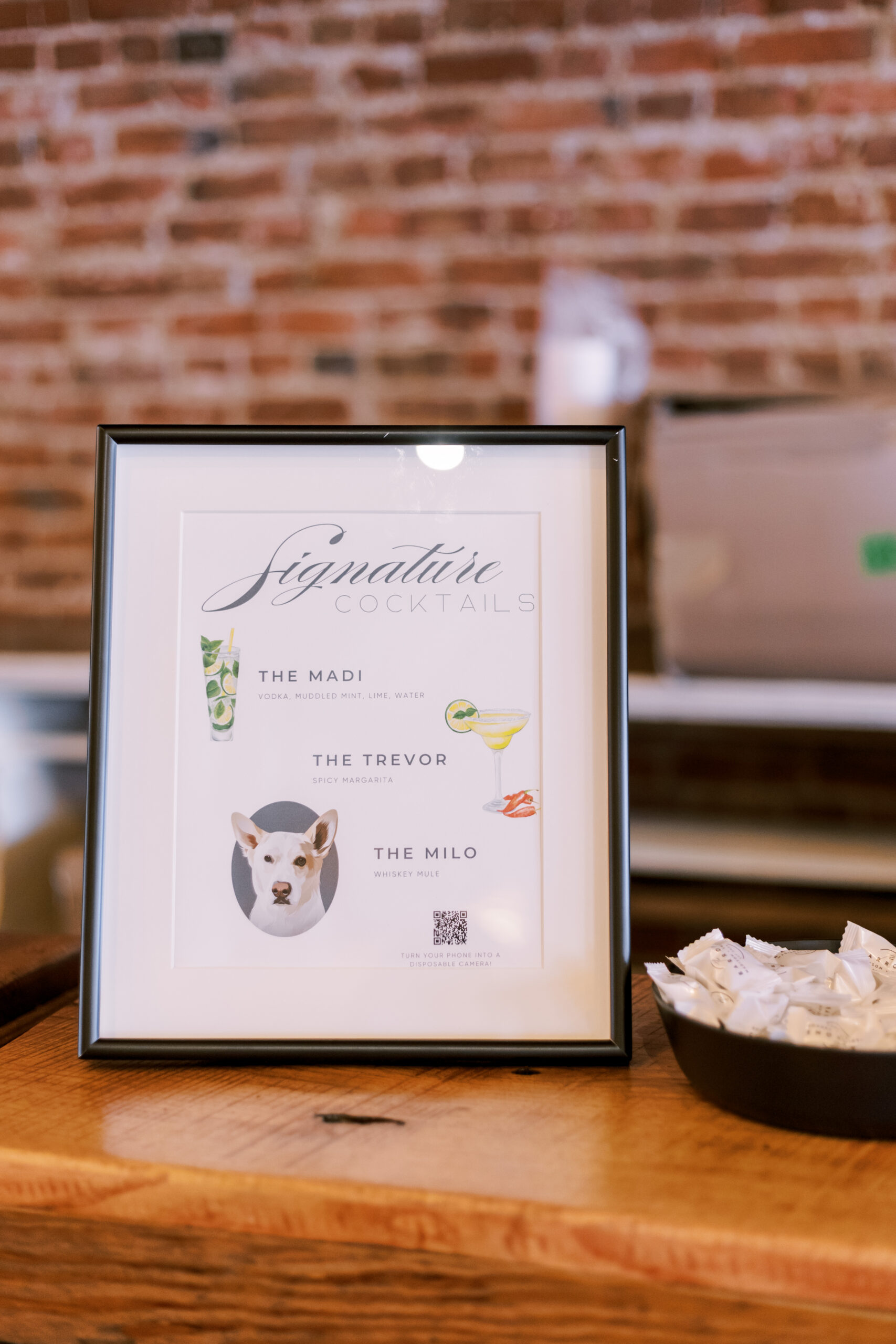 Framed wedding signature cocktail sign displayed on a wooden table at the reception.