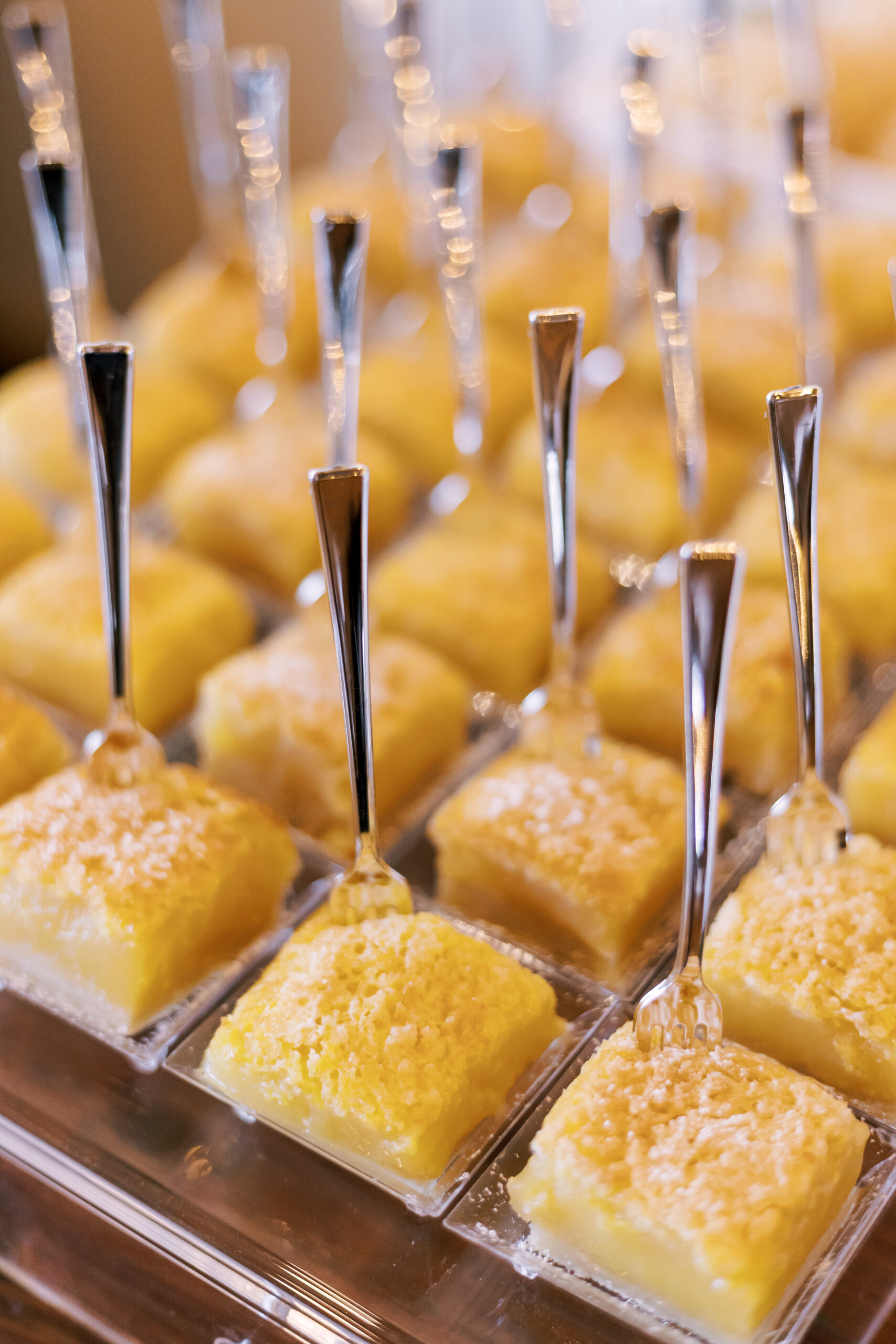 Small lemon dessert squares topped with powdered sugar and served with mini forks.