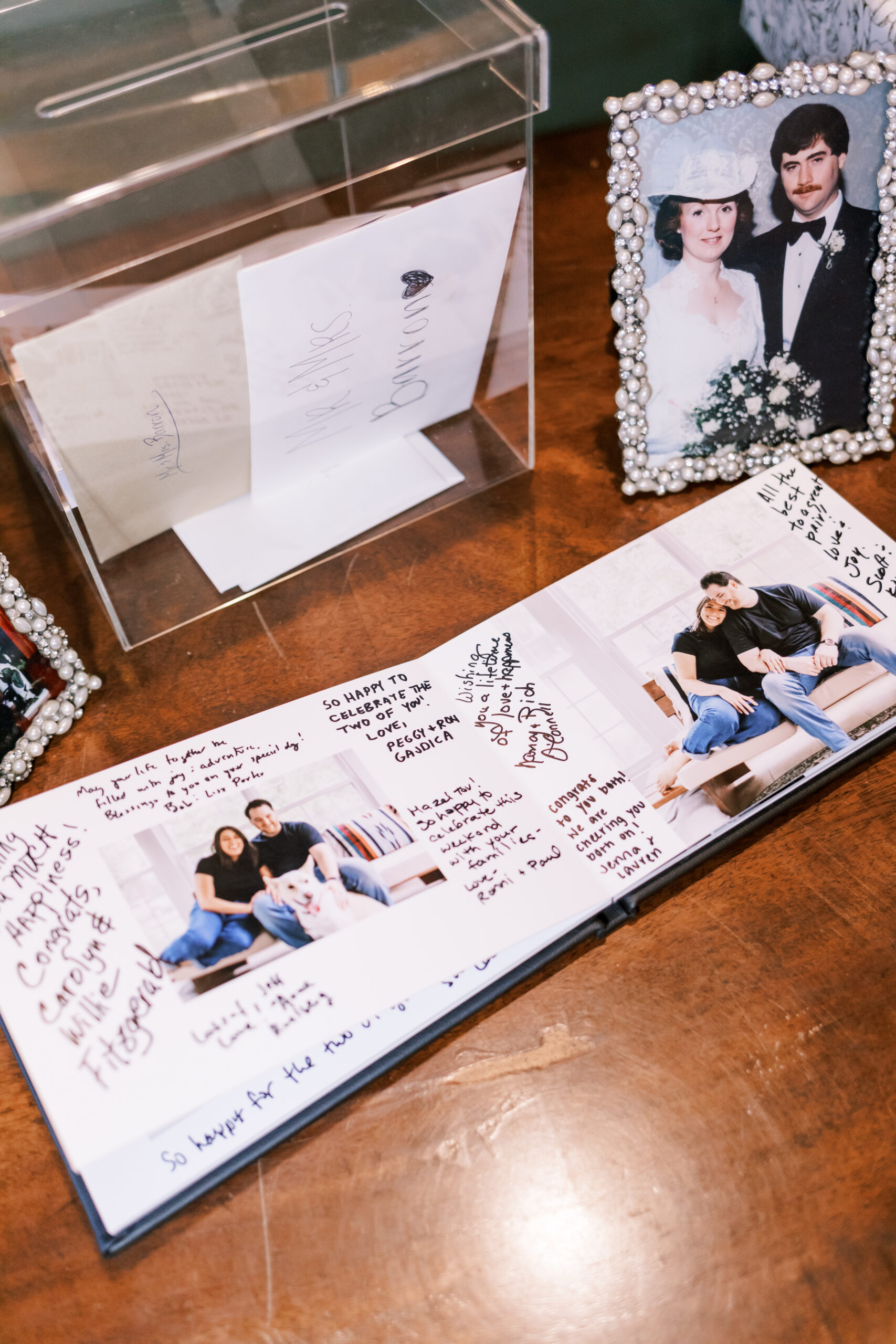 Wedding guestbook with handwritten notes displayed beside framed family photos and a card box.