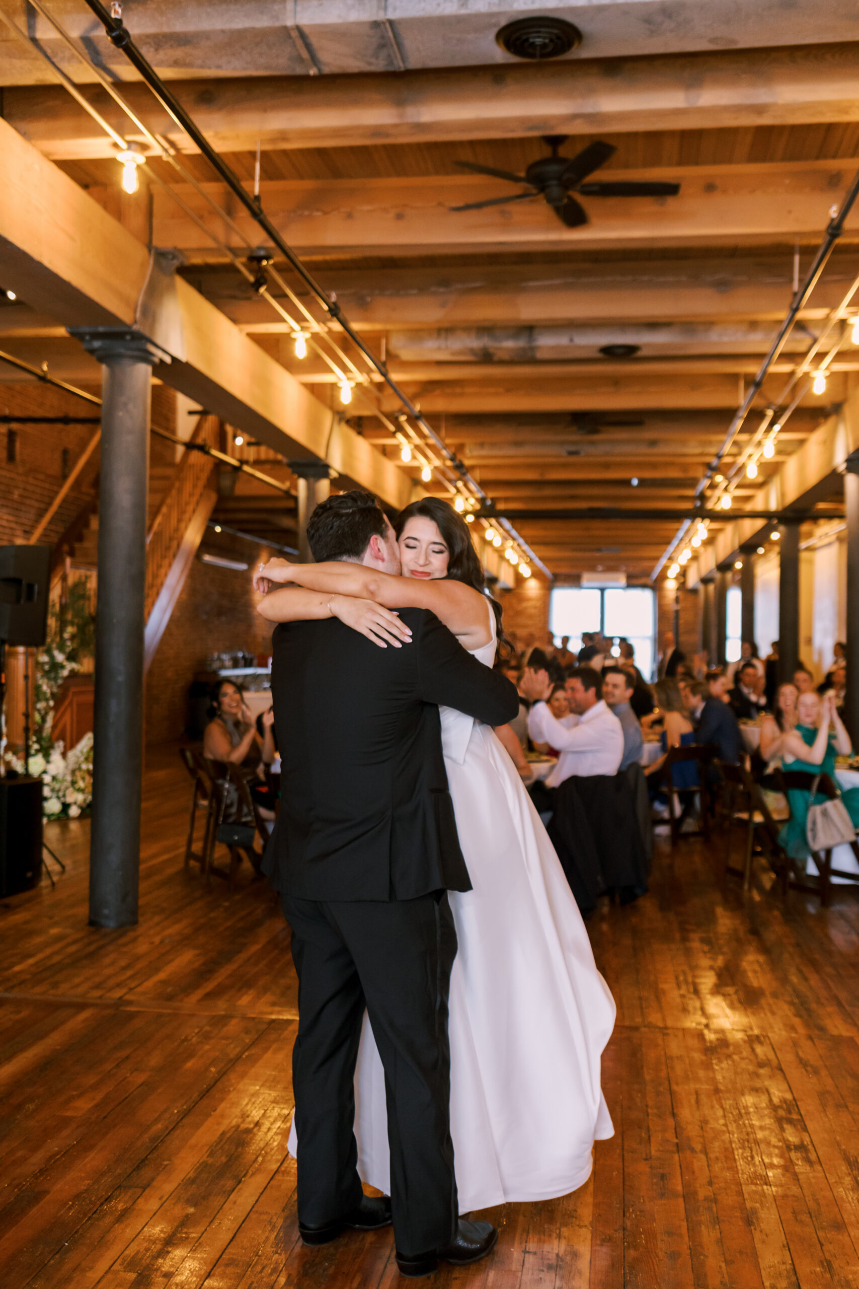 Bride hugging the groom on the dance floor as guests applaud during the reception.