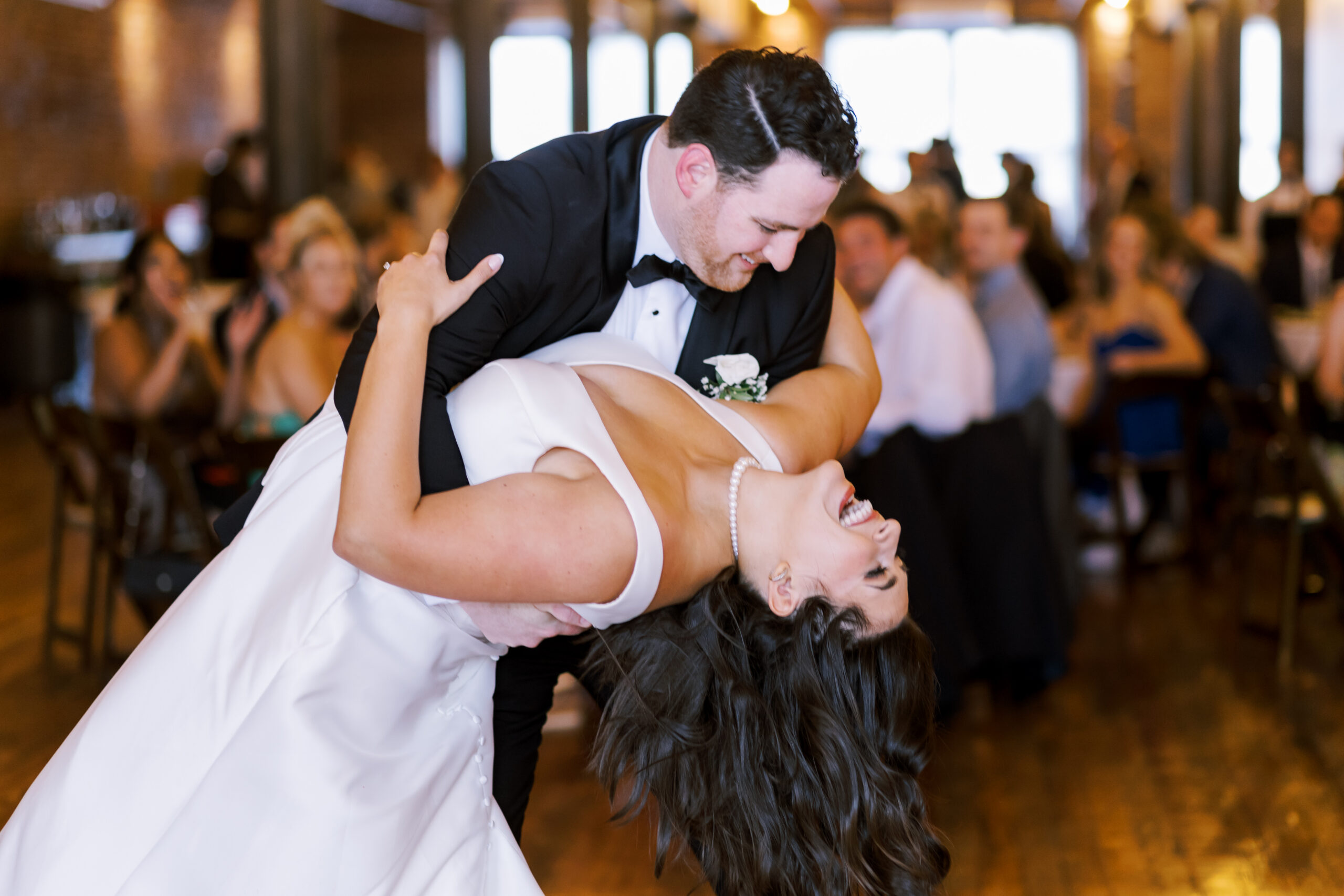 Groom dipping the bride during a dance while guests watch from their tables.