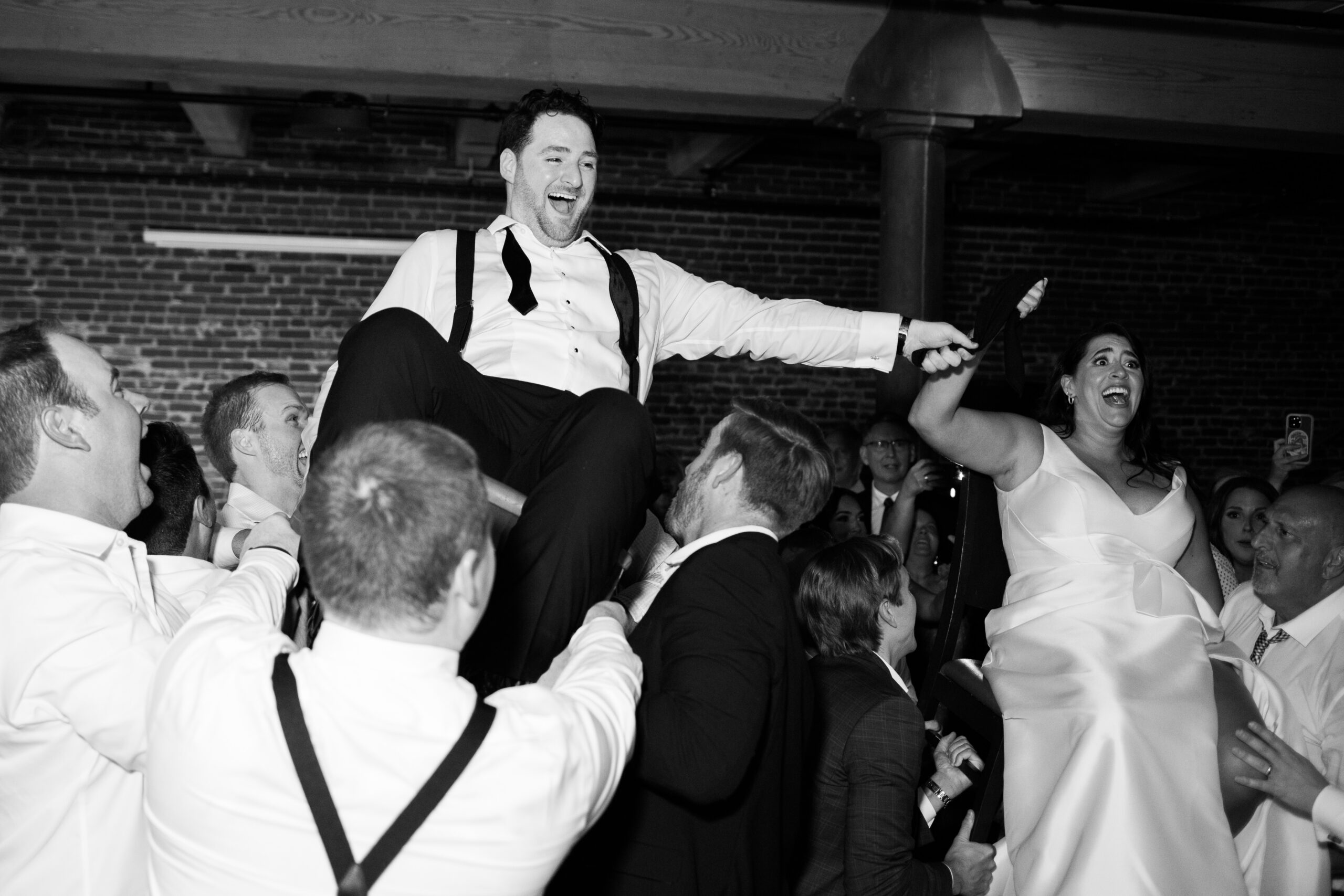 Bride and groom lifted on chairs by guests during a lively reception tradition.