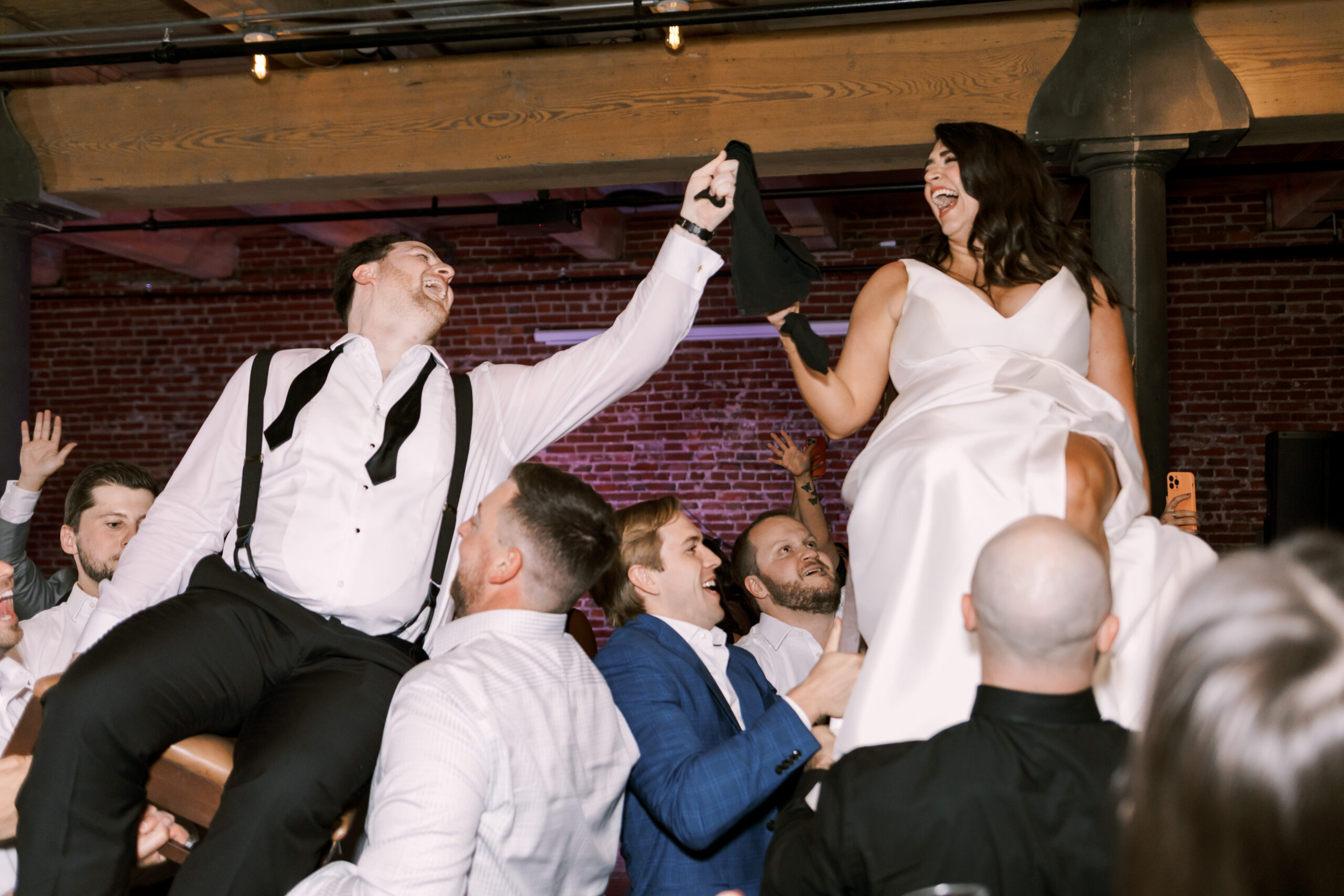 Bride and groom raised on chairs while holding hands during a wedding reception celebration.