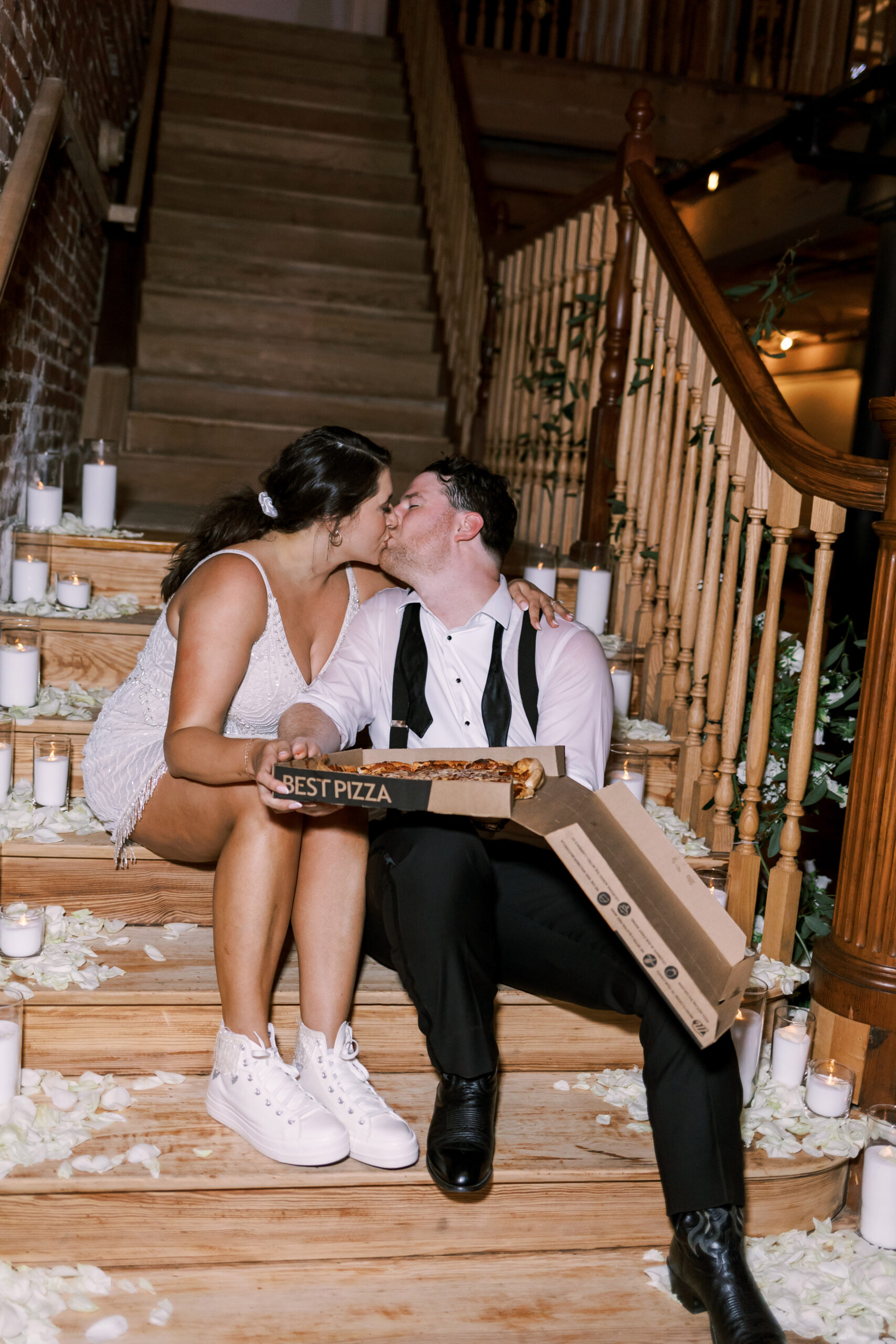 Bride and groom kissing on candlelit stairs, sharing a pizza box labeled "Best Pizza"