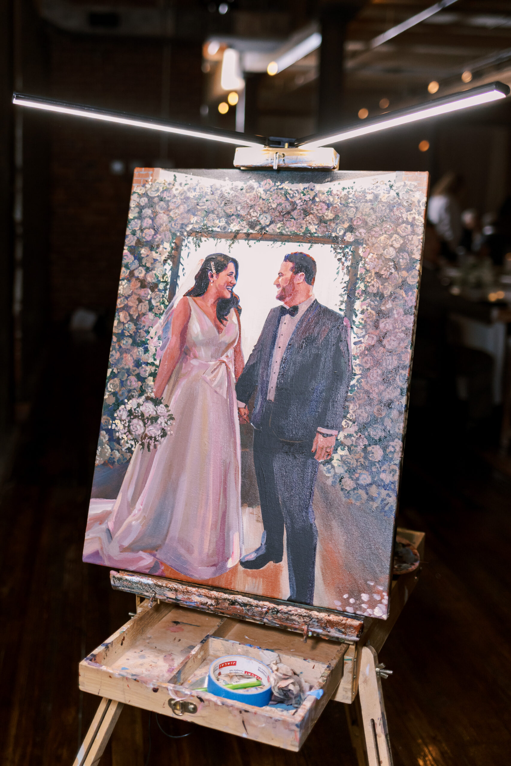 Live wedding painting on an easel depicting the bride and groom at the altar surrounded by flowers