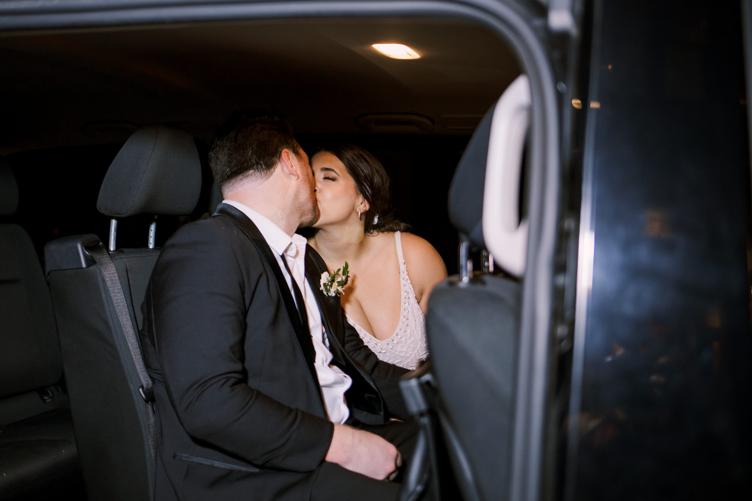 Bride and groom kissing in the back seat of a dark vehicle