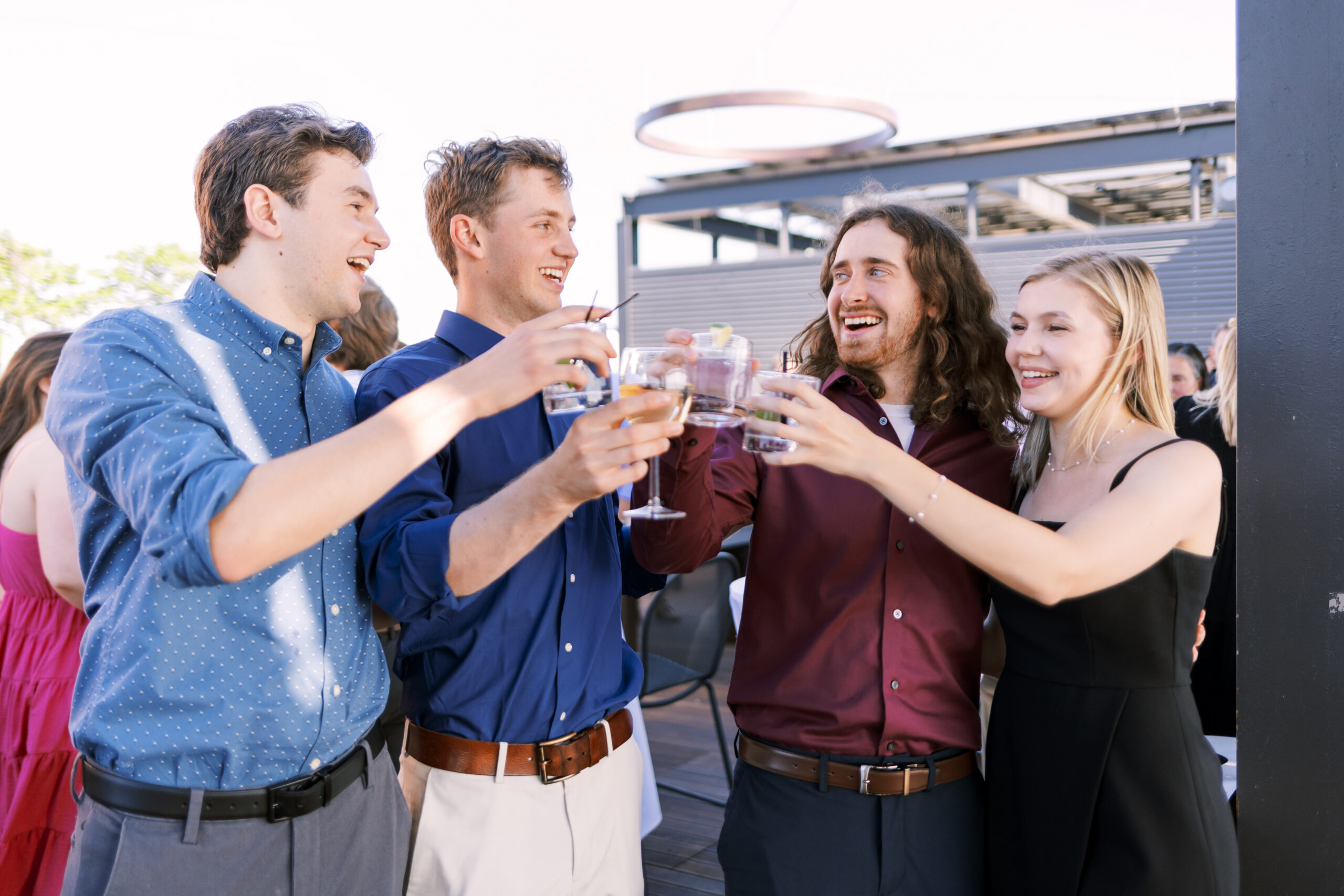 Group of guests clinking cocktails together on a rooftop terrace during an outdoor evening celebration.