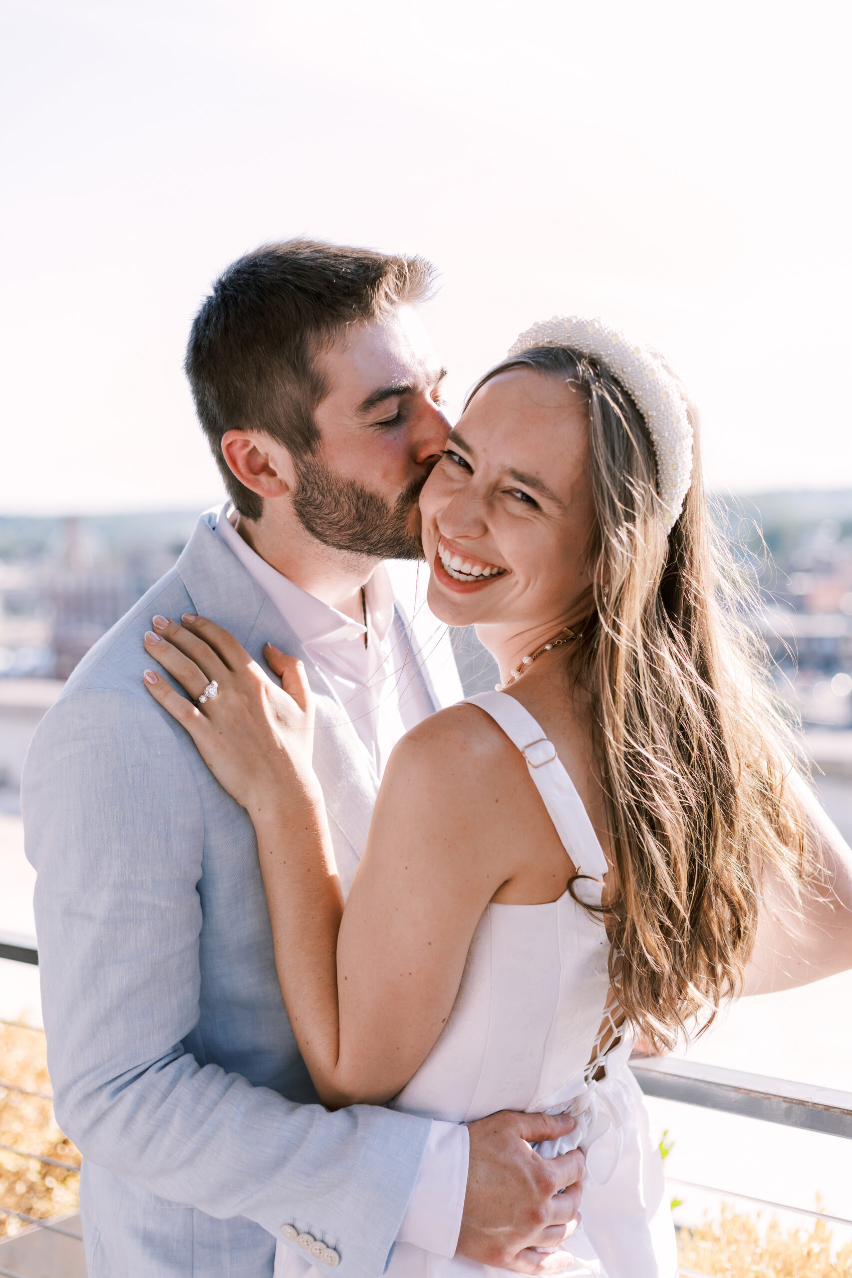 Close-up of a couple embracing as one kisses the other’s cheek on a rooftop at sunset.