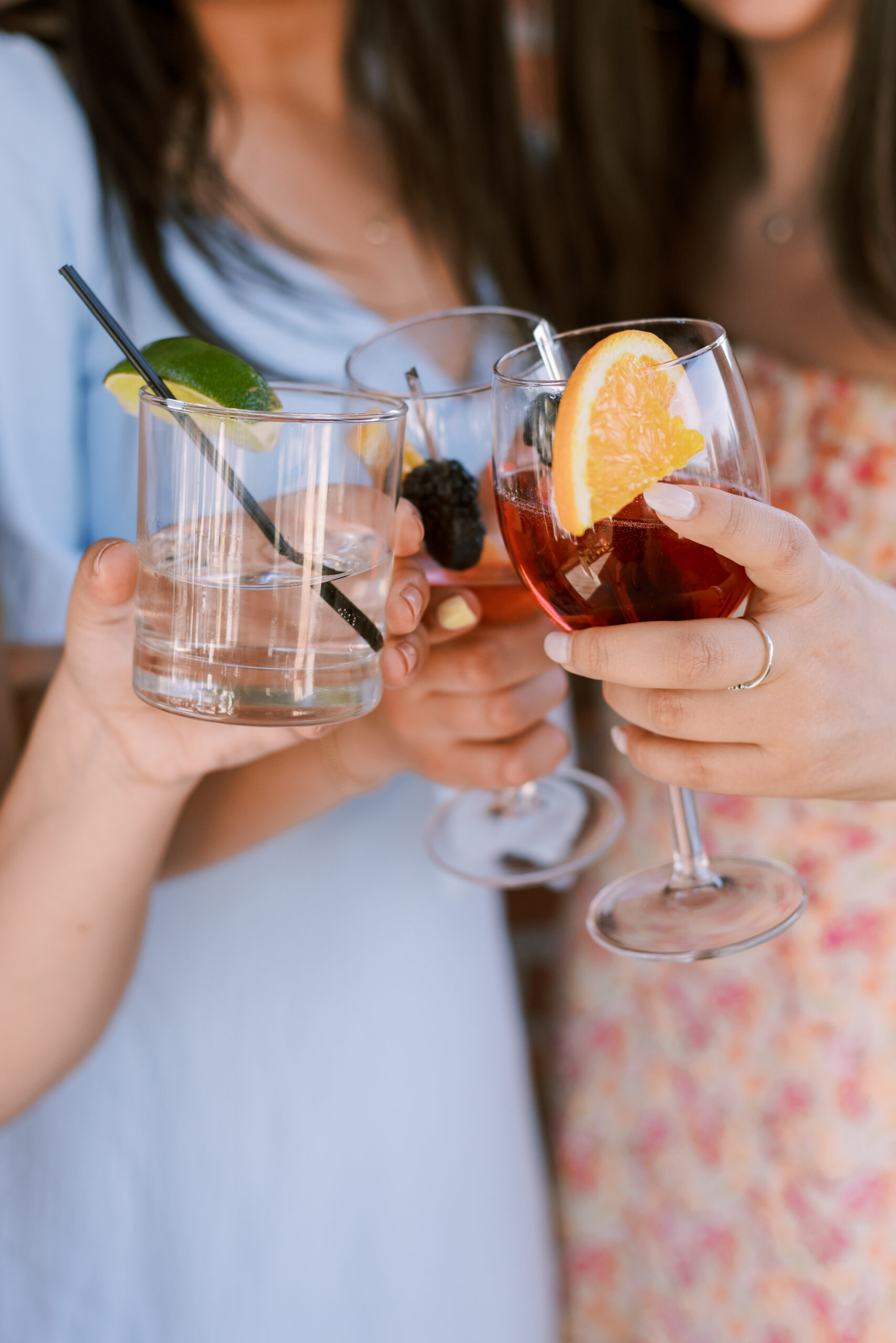 Hands holding cocktails with citrus garnishes as guests toast during a rooftop celebration.