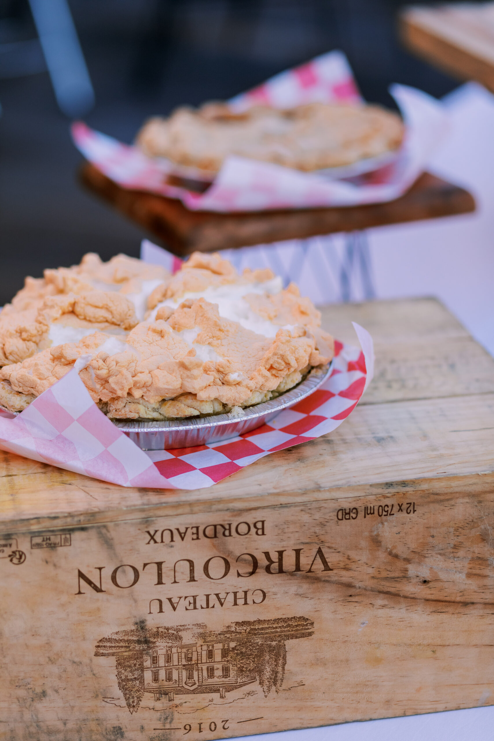 Whole pies with crumb topping displayed on wooden stands lined with red checkered paper at an outdoor dinner.