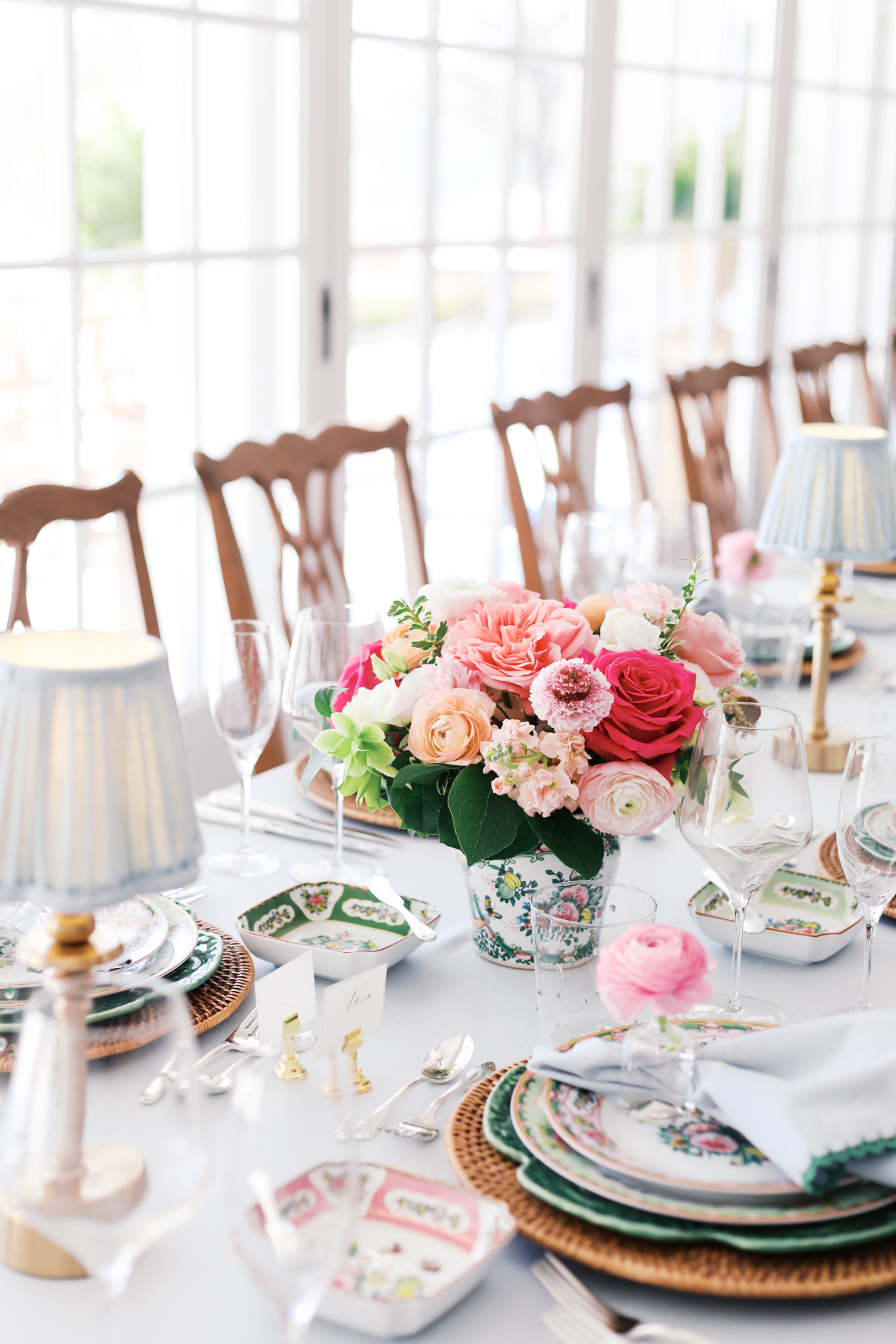 Elegant reception table with floral centerpiece, patterned china, and glassware in bright sunlit dining room.