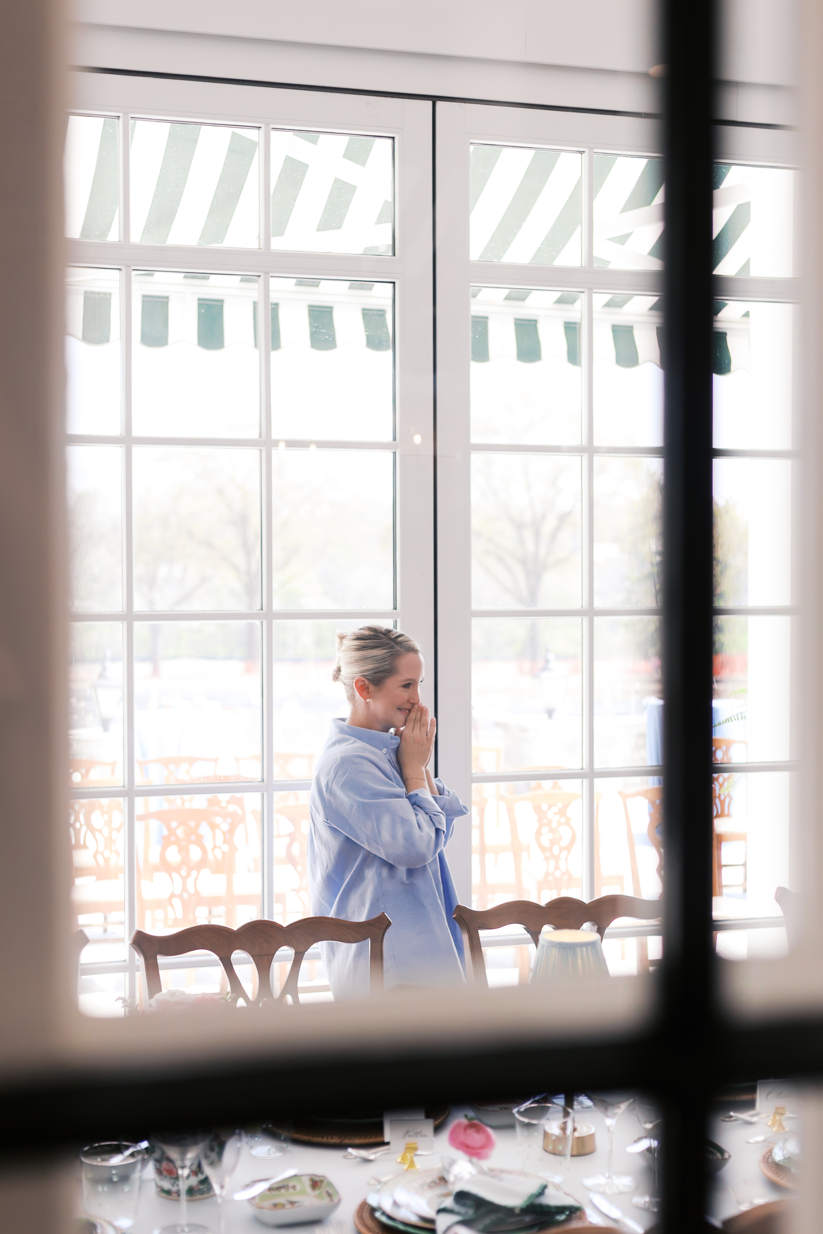 Woman in blue shirt stands by window, hands clasped, looking at decorated reception table.