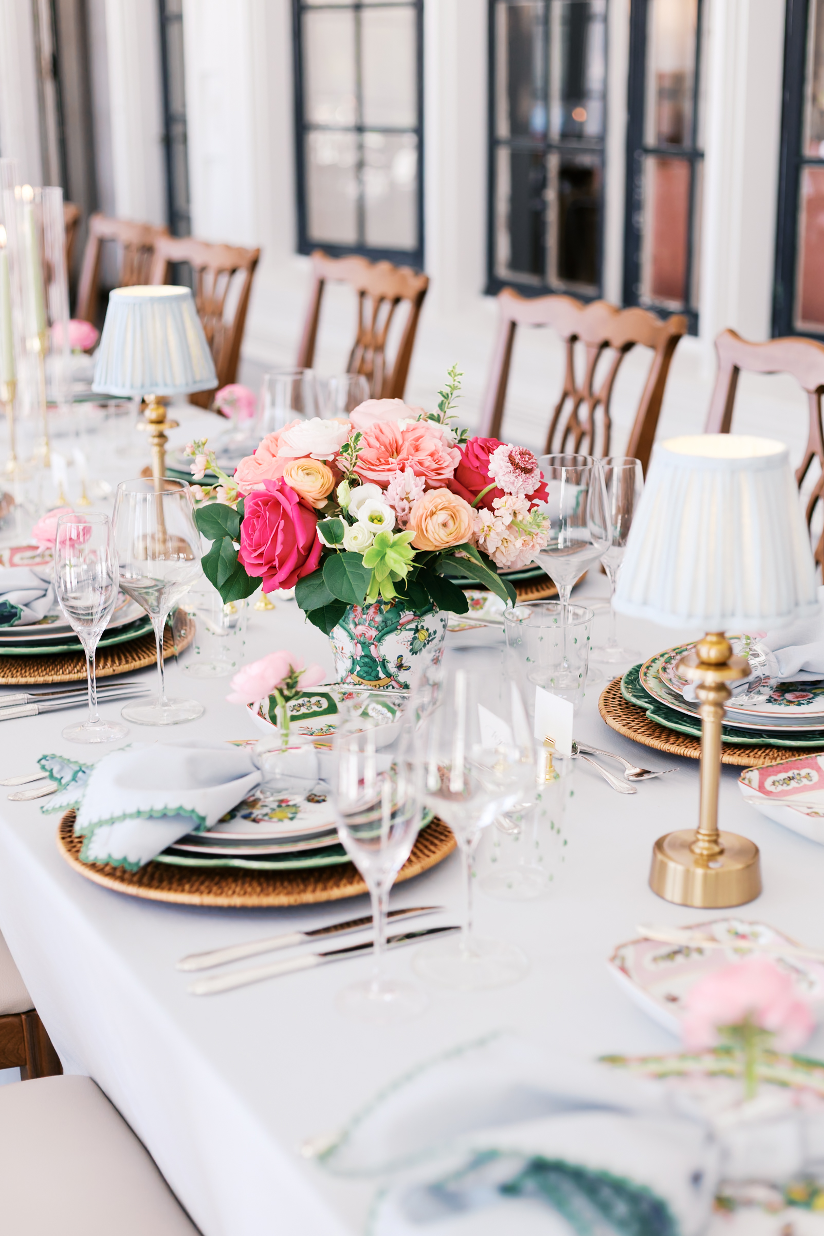 Close view of floral centerpiece with pink and coral blooms on styled reception table with glassware.