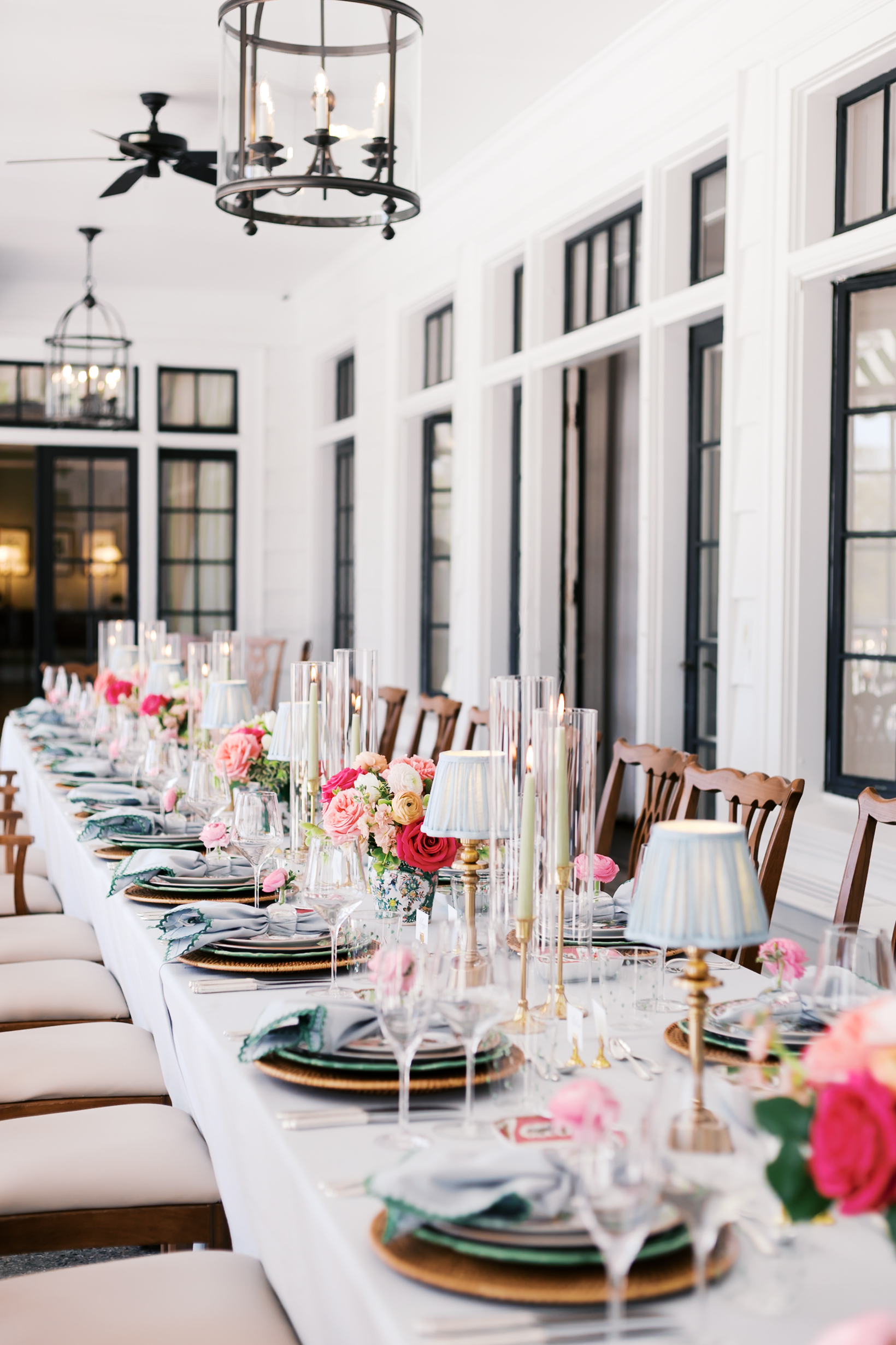 Long wedding table with candles, florals, and place settings in airy white reception space.