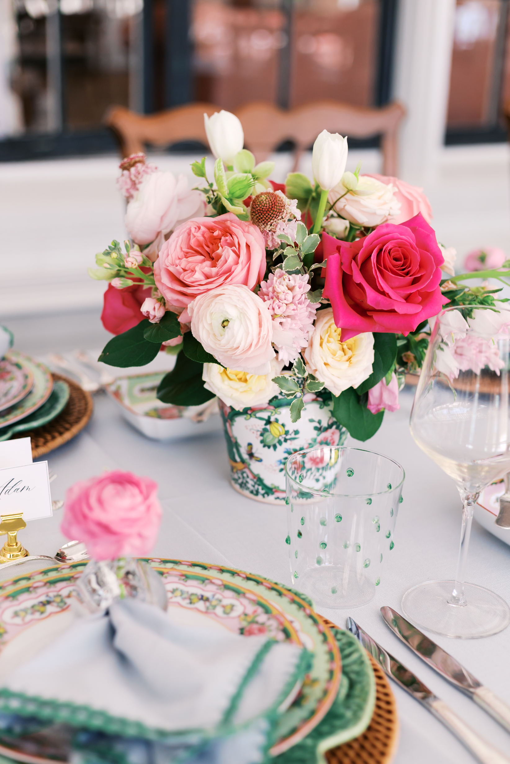 Close-up of colorful floral arrangement with roses and ranunculus on elegantly set table.