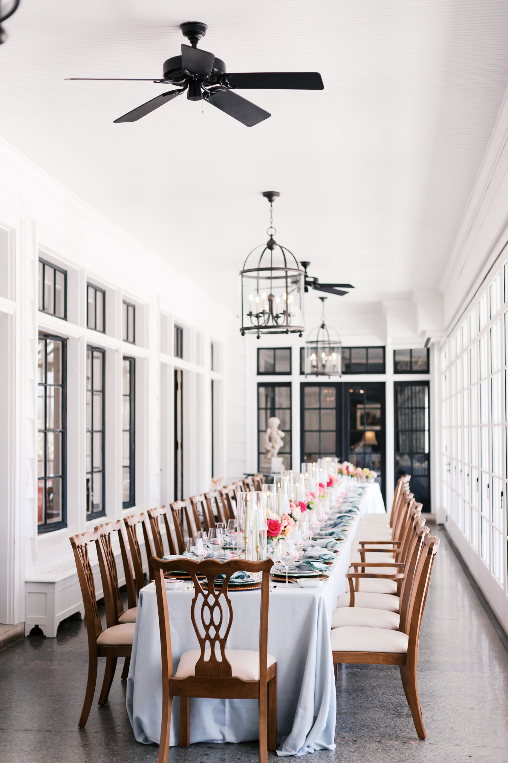 Long wedding table with candles, florals, and place settings in white reception space.