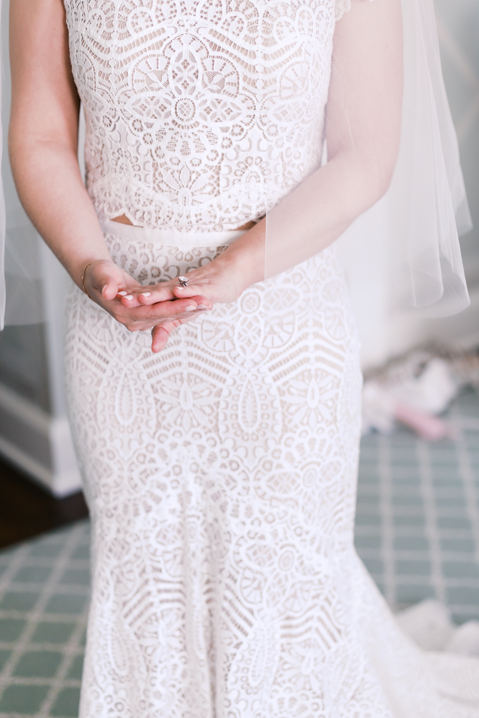 Close-up of bride’s lace dress and hands showing ring detail.
