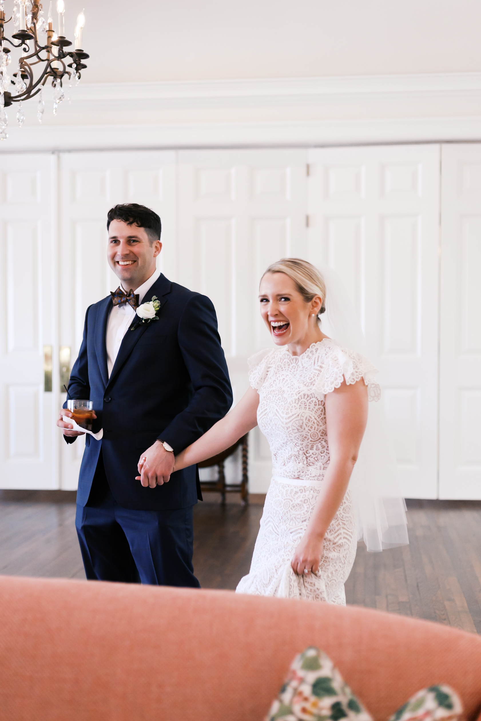 Bride and groom walking hand in hand indoors, smiling during wedding celebration.