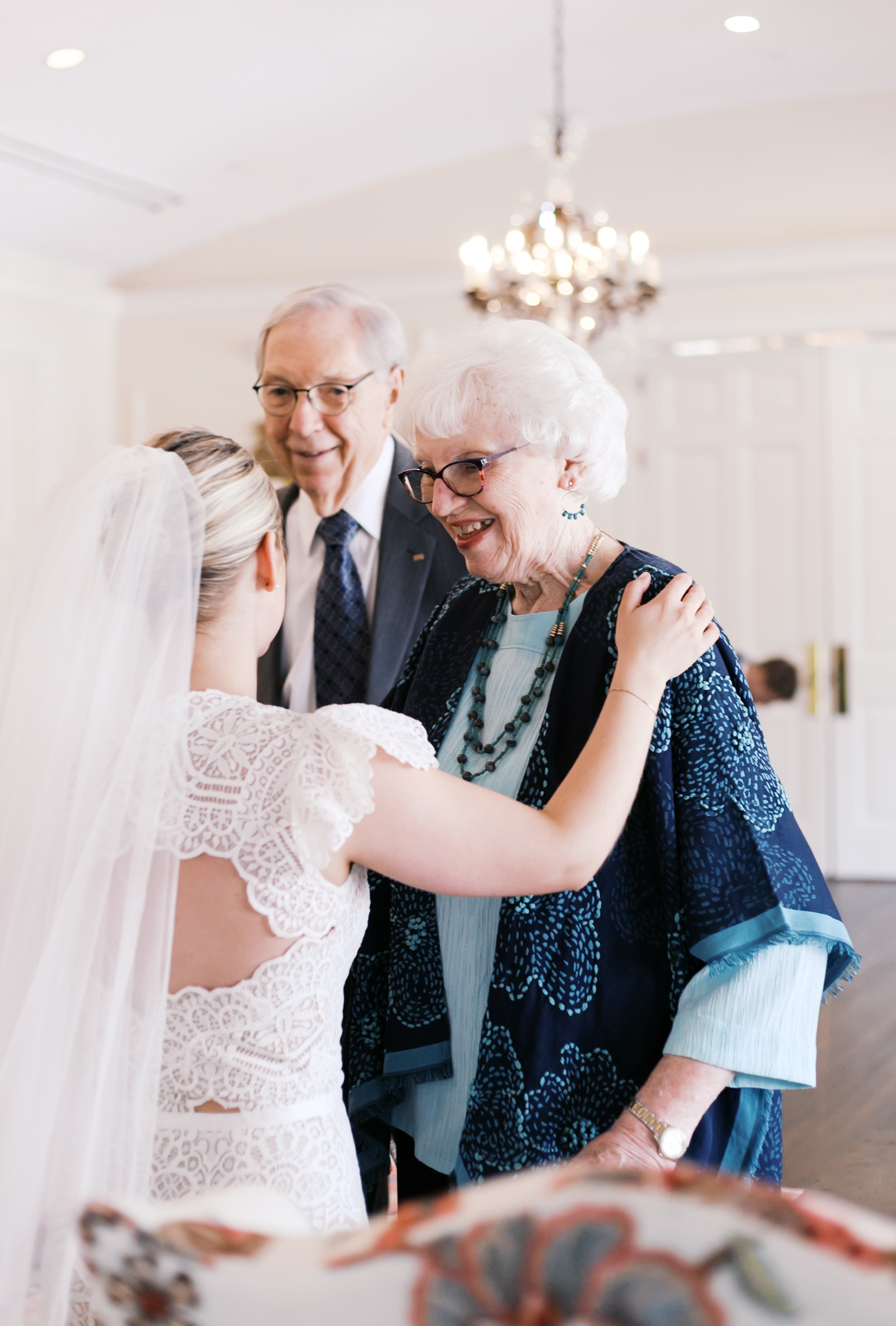 Bride embraces older couple, sharing a warm greeting during wedding reception.