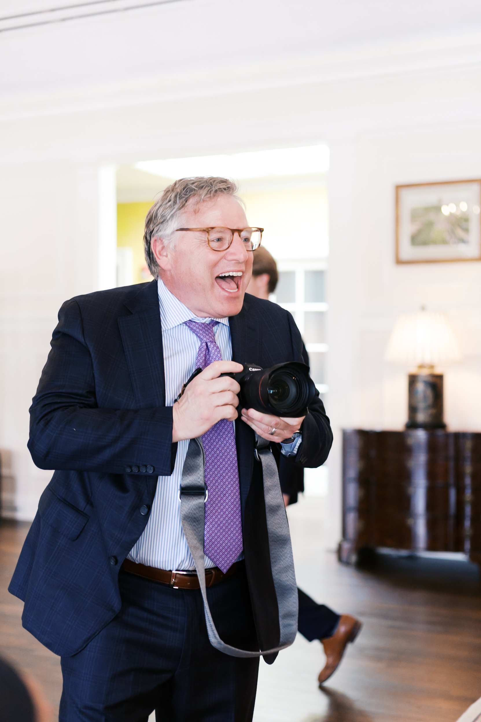 Guest in suit holding camera and smiling while taking photos at wedding.