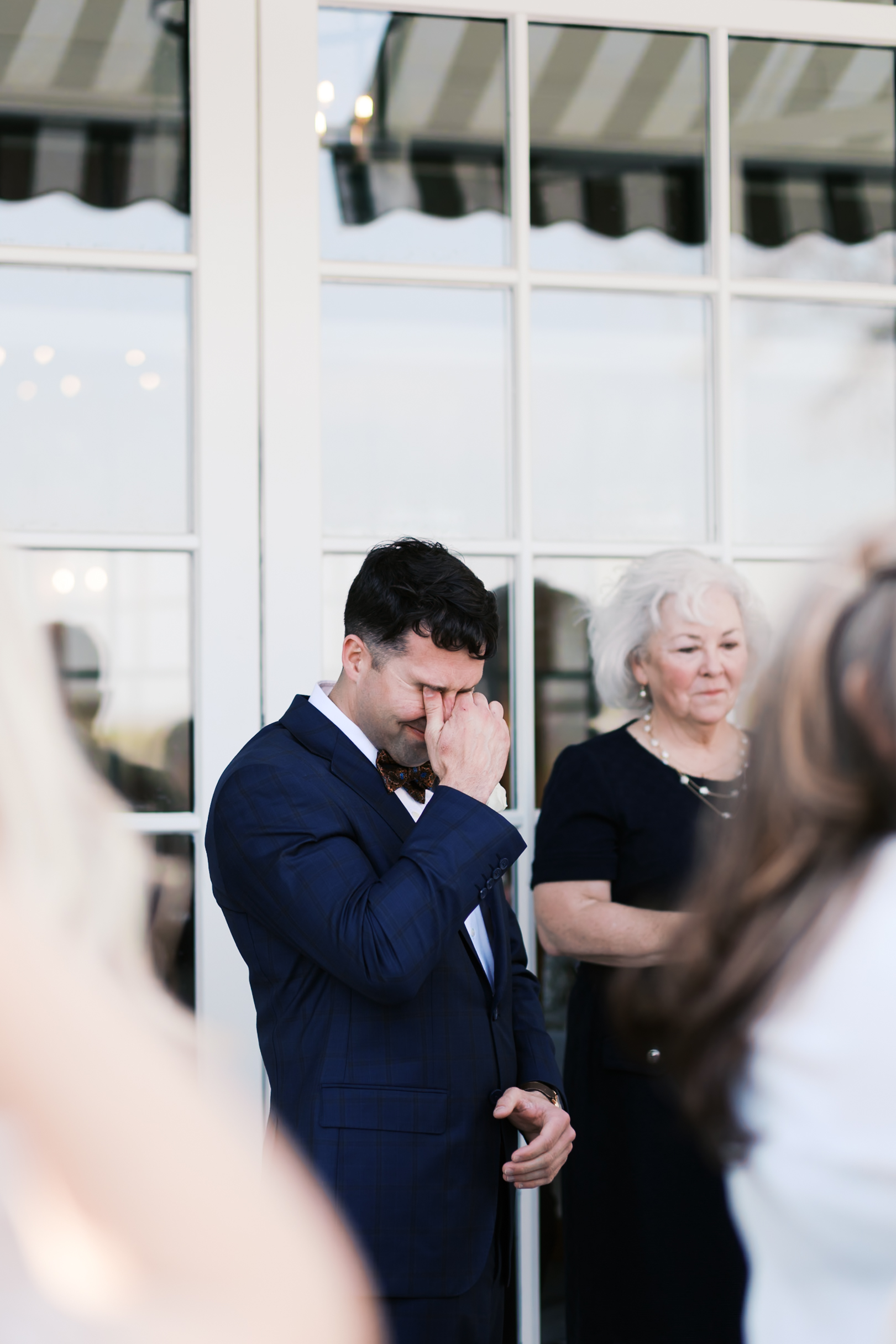 Groom in navy suit wiping his eye during outdoor wedding ceremony