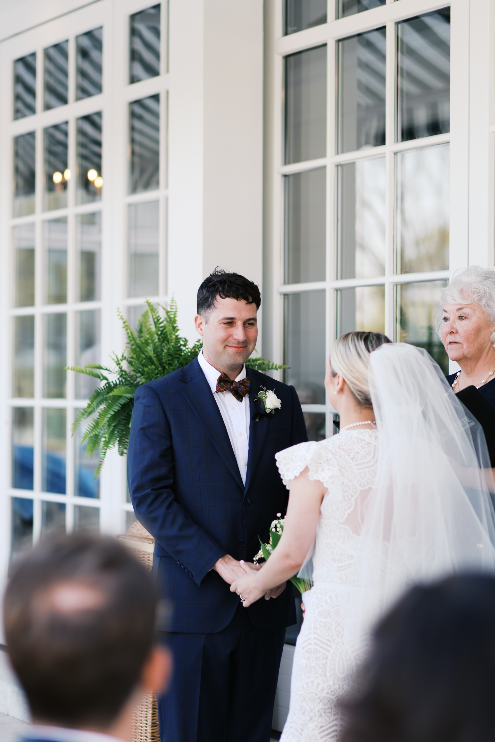 Bride and groom holding hands during ceremony in front of white building with large windows