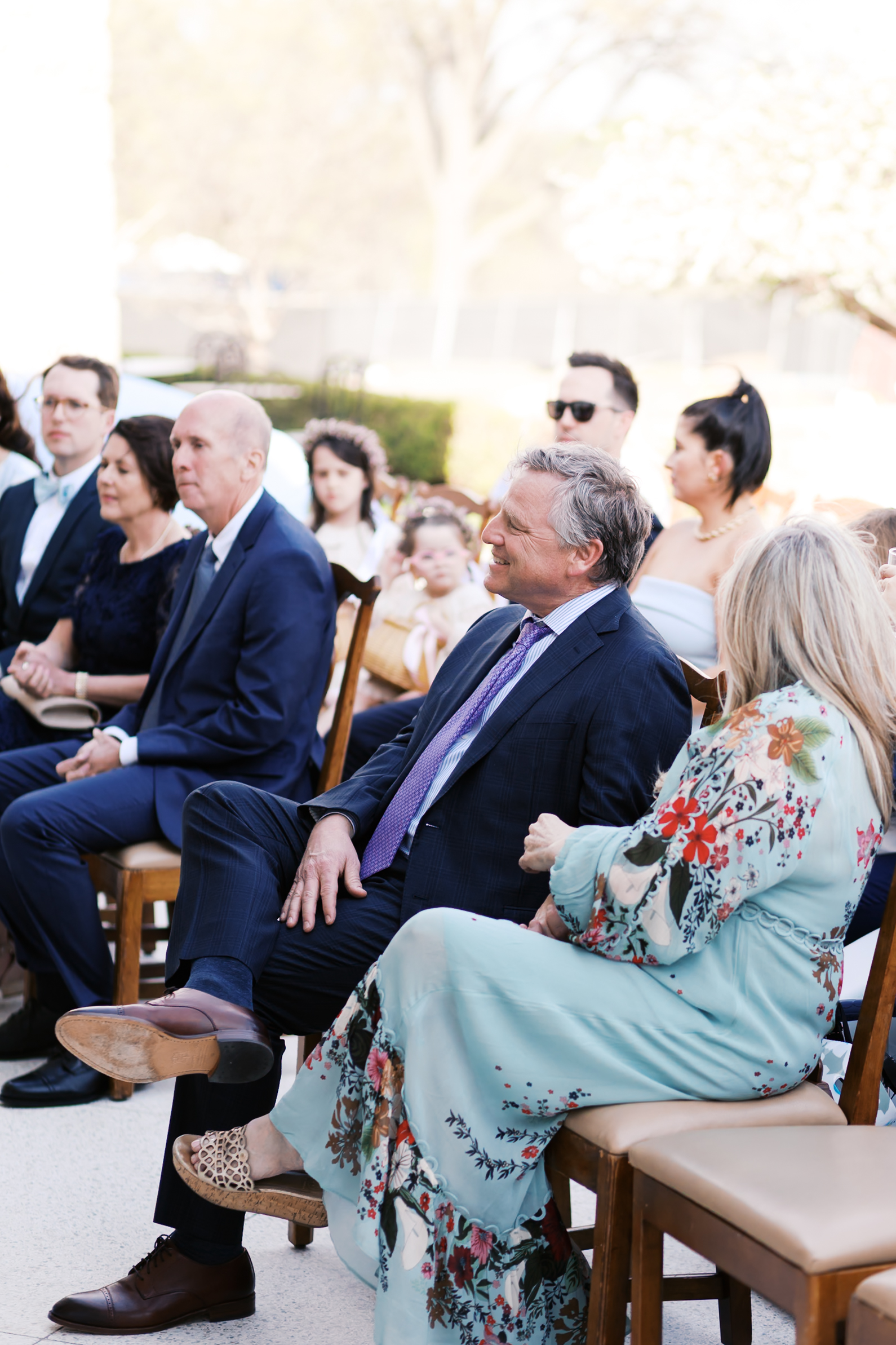 Wedding guests seated outdoors watching ceremony, dressed in formal attire