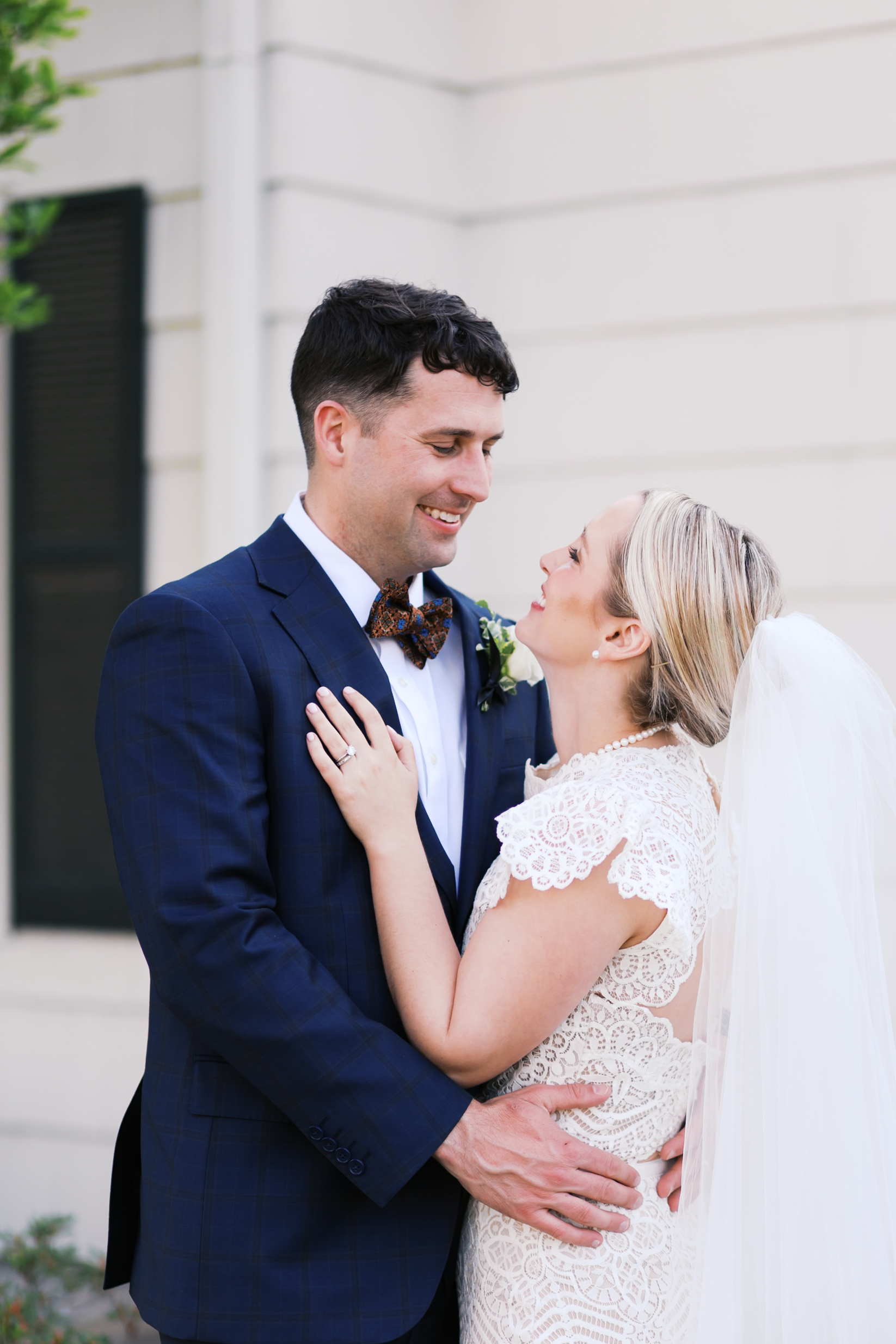 Bride and groom embracing outdoors near white building