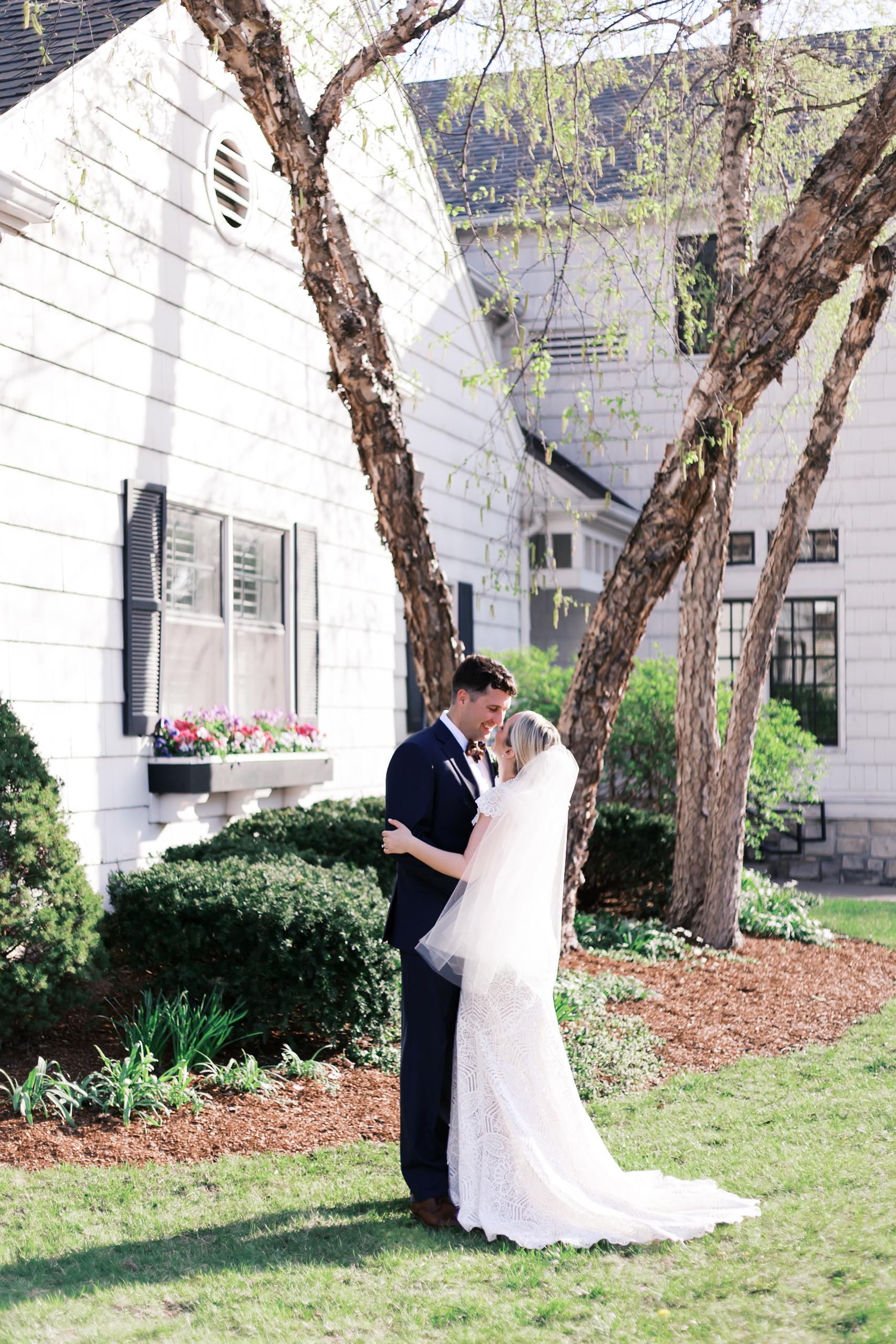 Bride and groom embracing outdoors near trees and white building