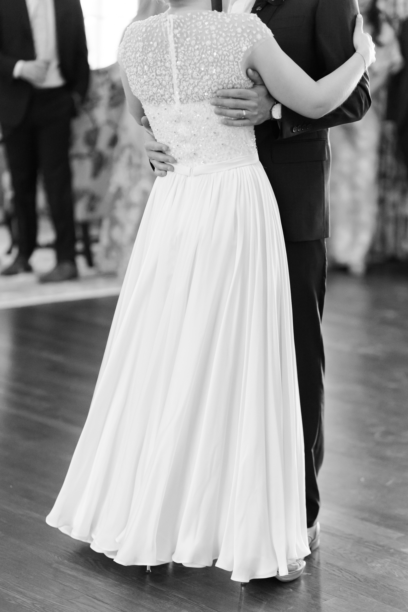 Close-up of bride and groom dancing, showing wedding dress and suit details
