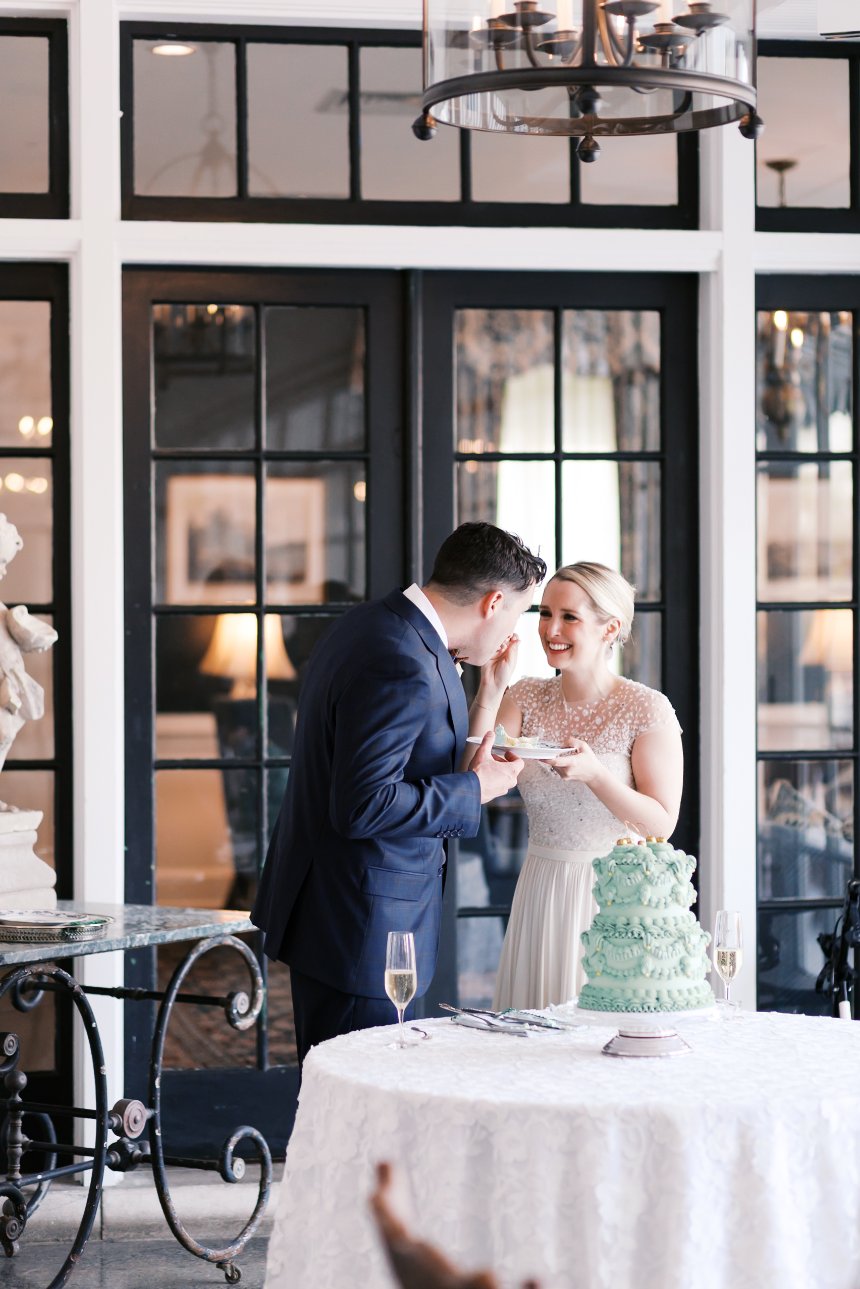 Bride feeding groom cake beside mint green wedding cake on table during reception
