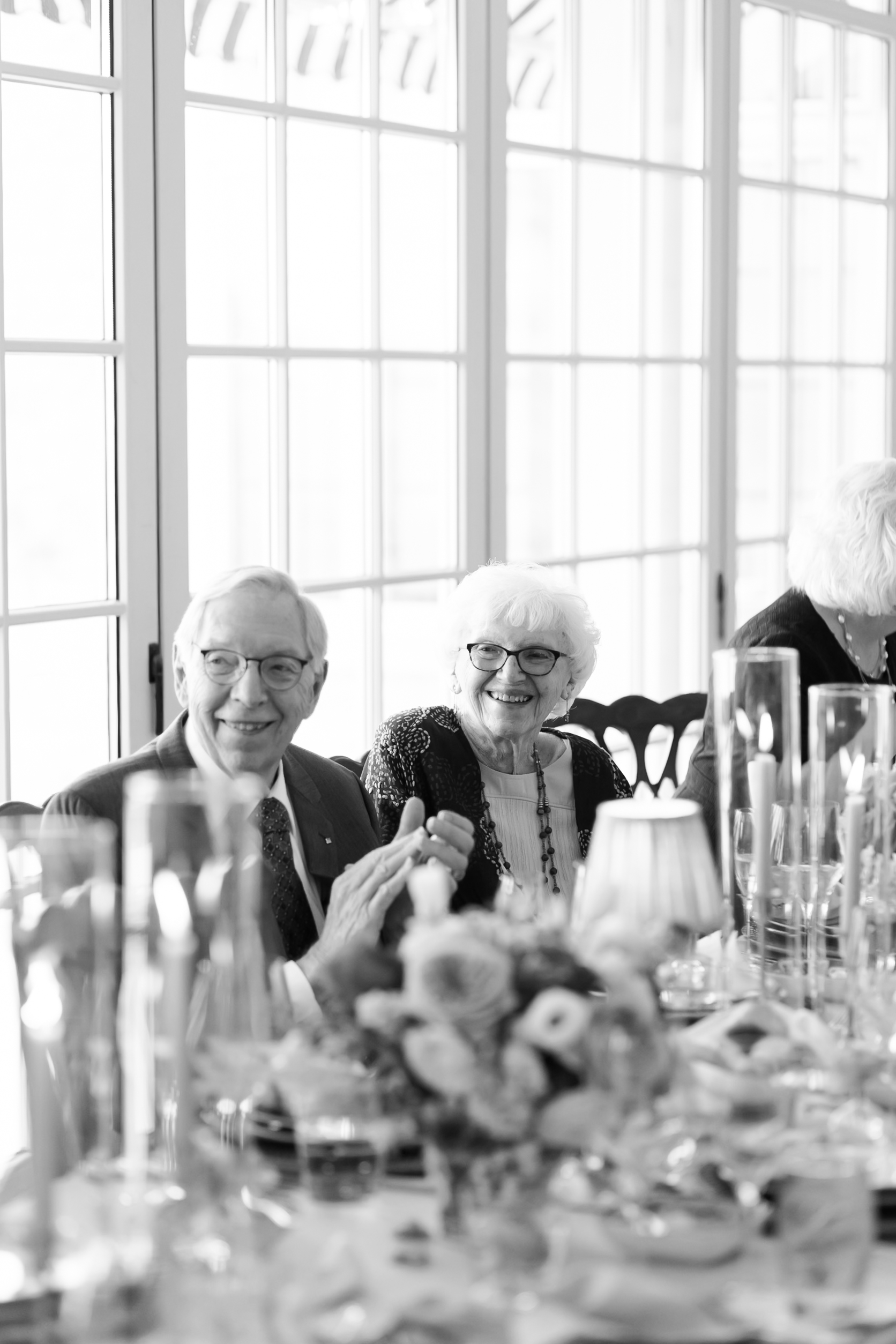 Elderly couple smiling and seated at decorated reception table with candles and flowers