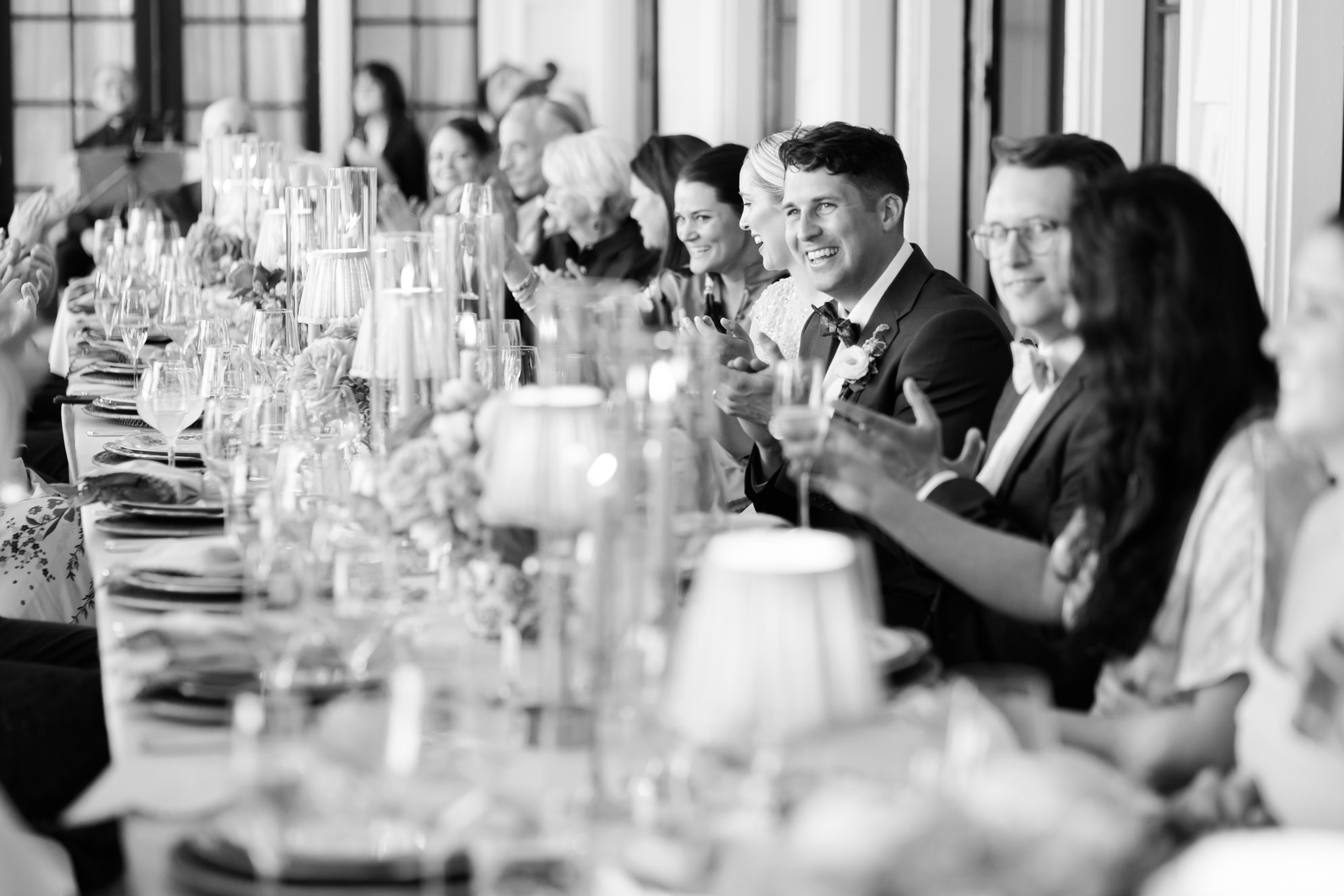 Wedding guests seated at long table applauding during reception dinner
