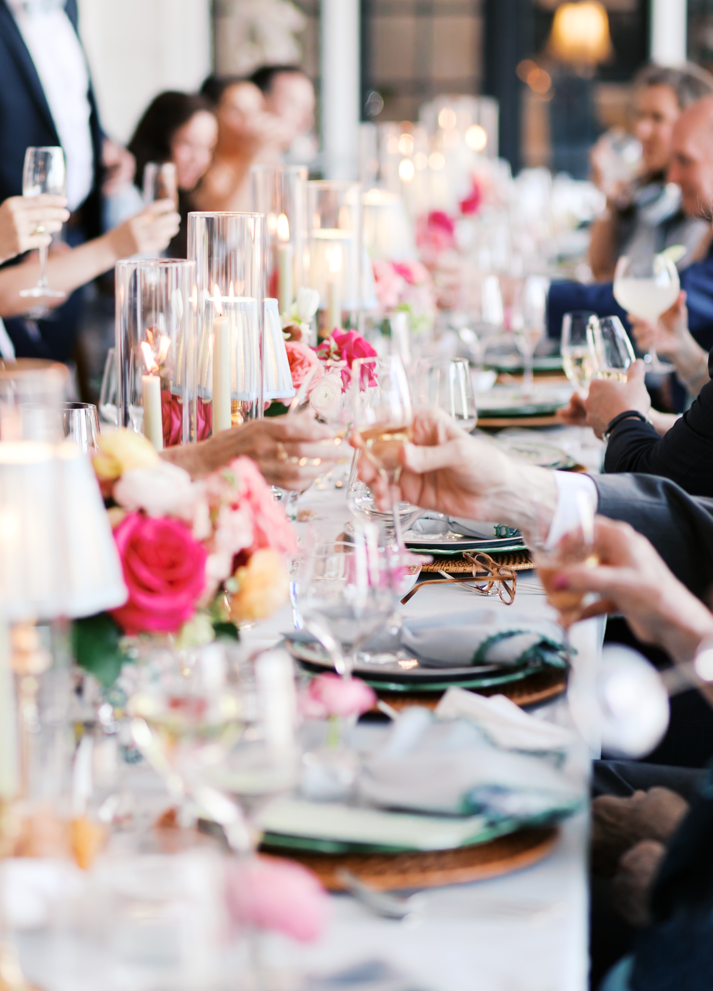 Guests raising glasses for toast at reception table with candles and floral centerpieces