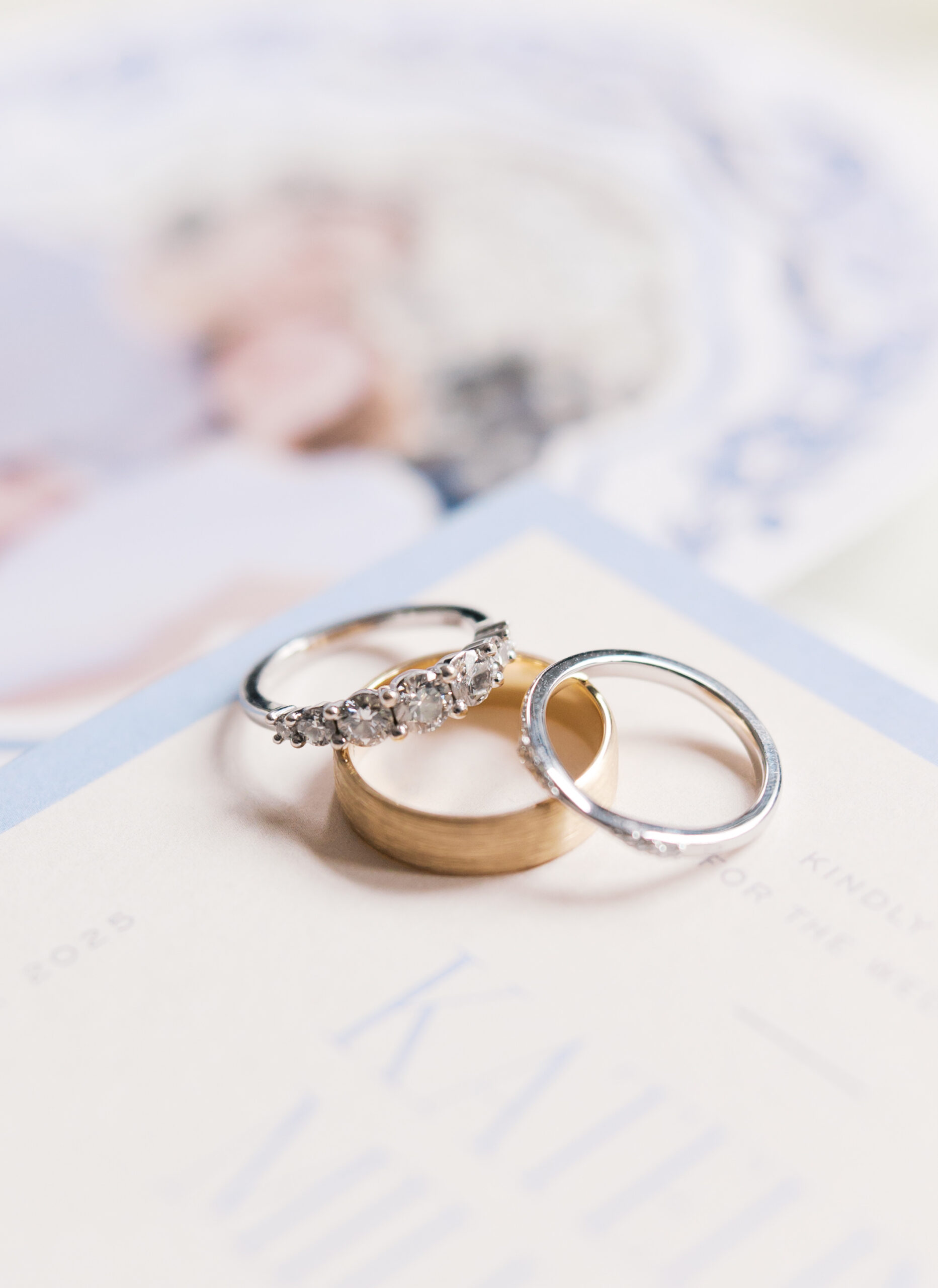 Diamond engagement ring and two wedding bands resting on a printed invitation suite
