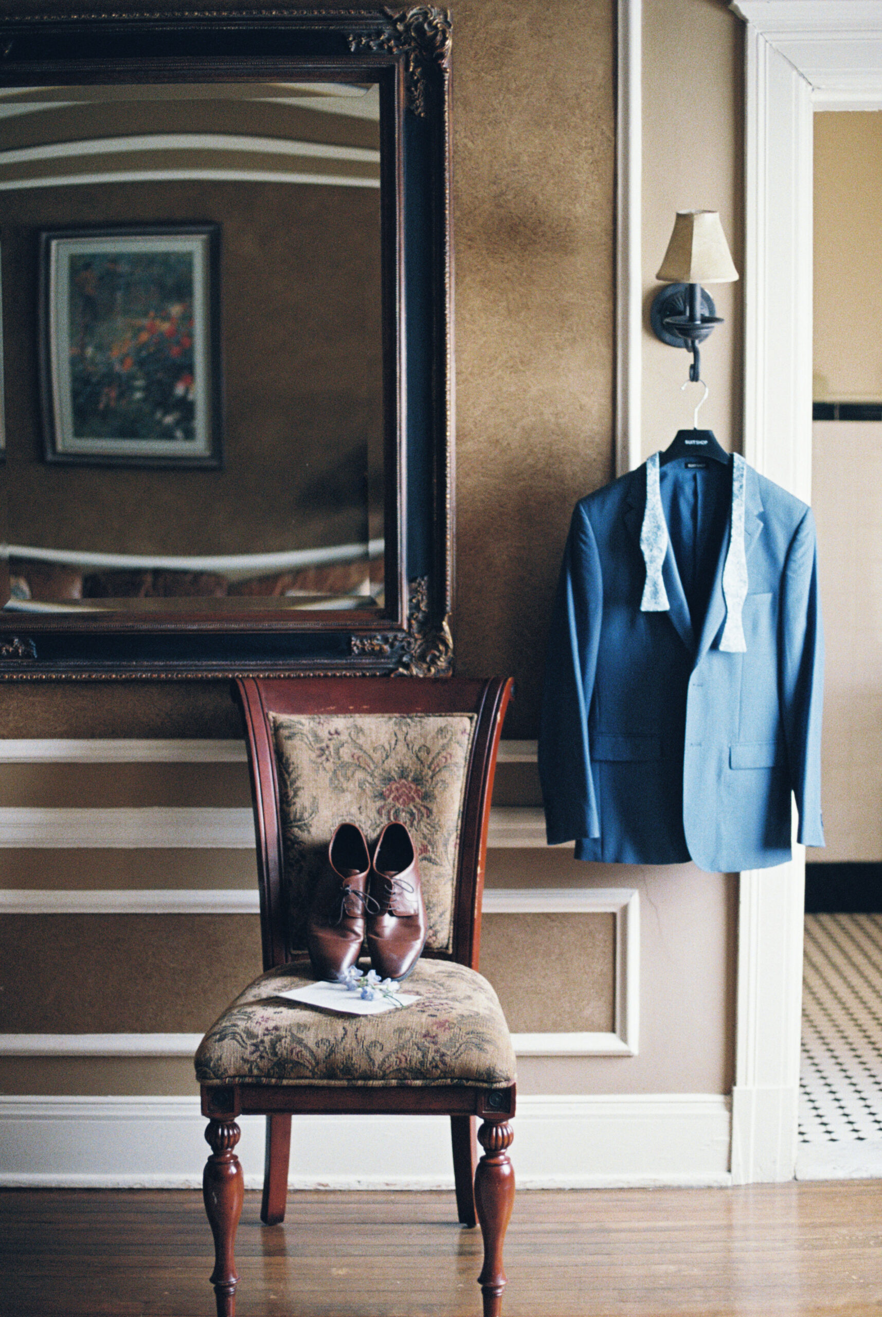 Blue suit jacket hanging on wall above brown shoes placed on an upholstered chair