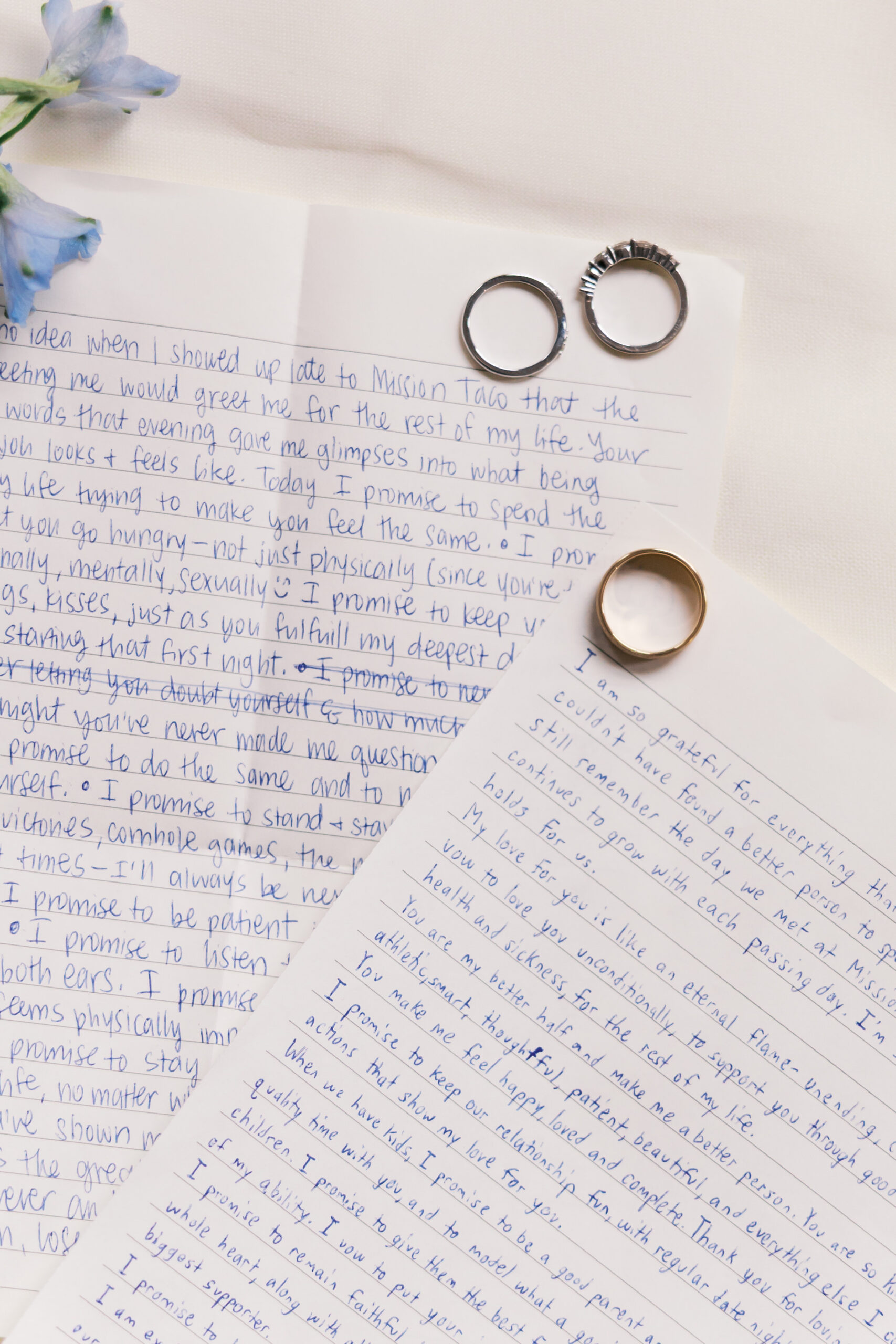 Wedding bands resting on handwritten vows with blue ink on white paper
