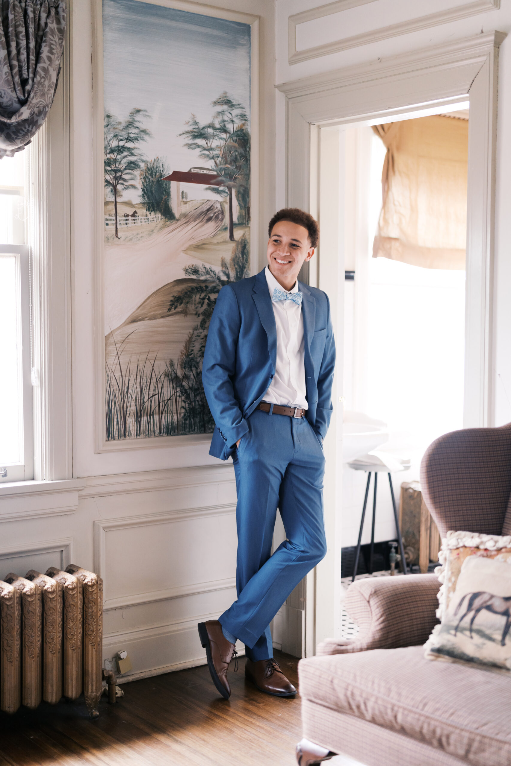 Groom in blue suit leaning casually in doorway with natural ligh