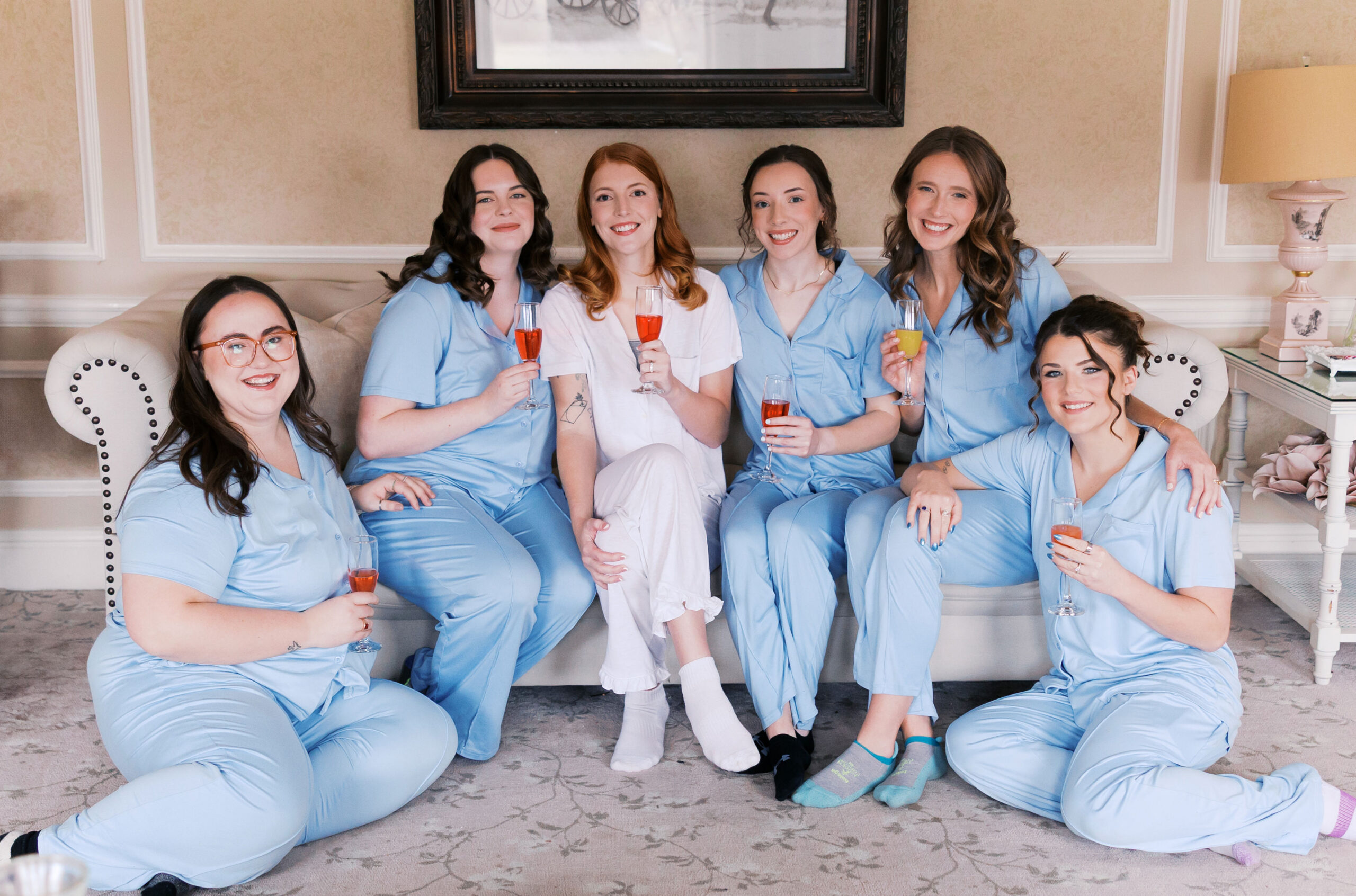 Group of women in matching blue pajamas sitting together holding drinks on a couch