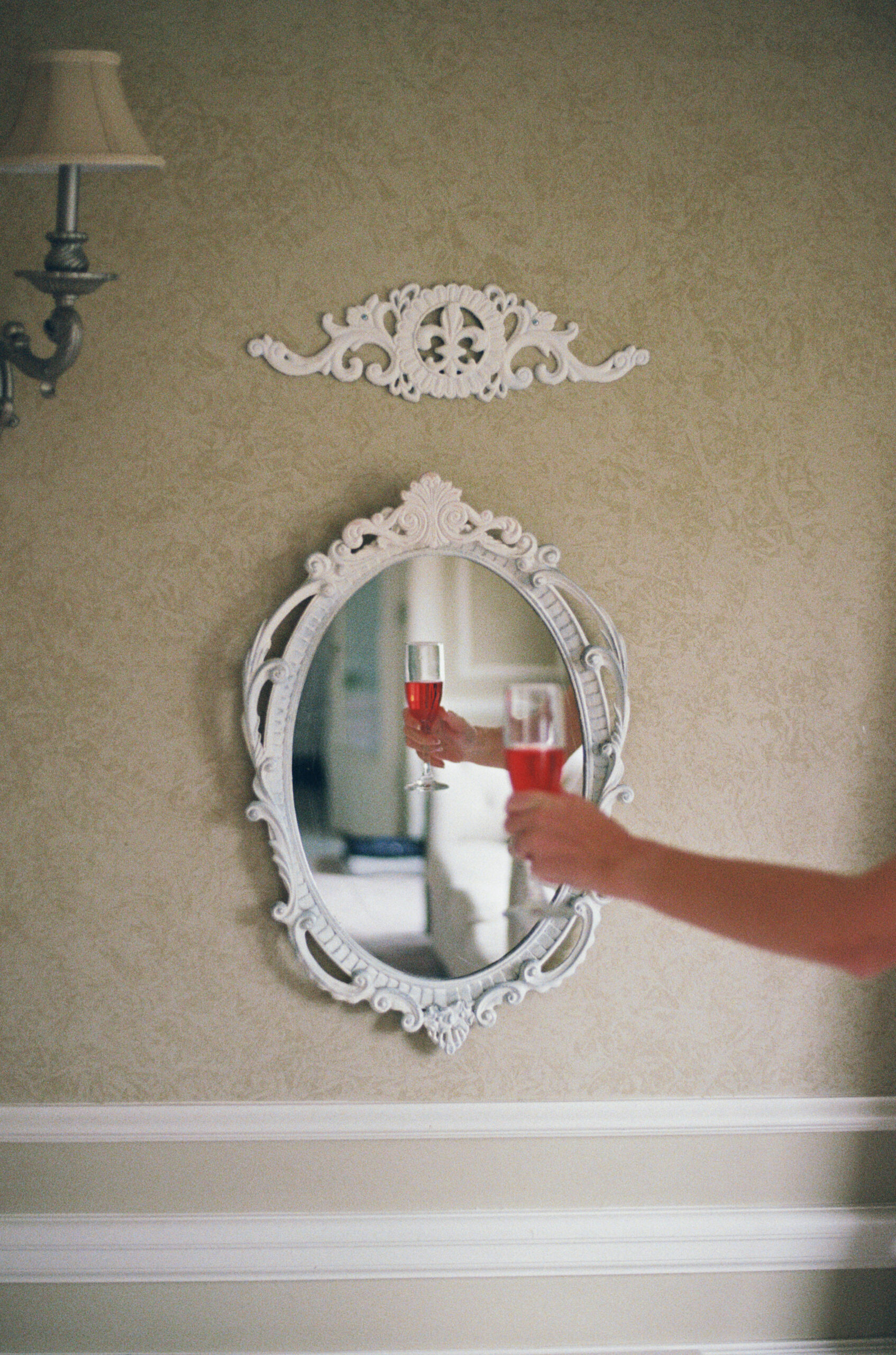 Hand holding glass of red drink reflected in ornate wall mirror