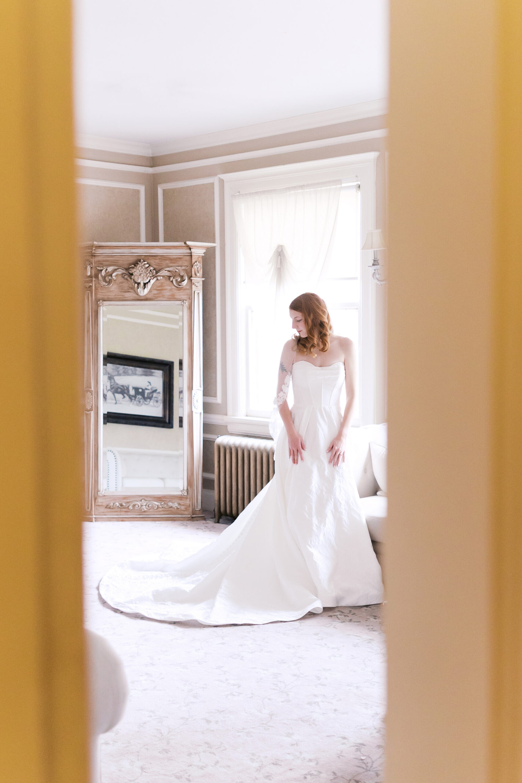 Bride standing in window light with long train, framed doorway view at Longview Mansion