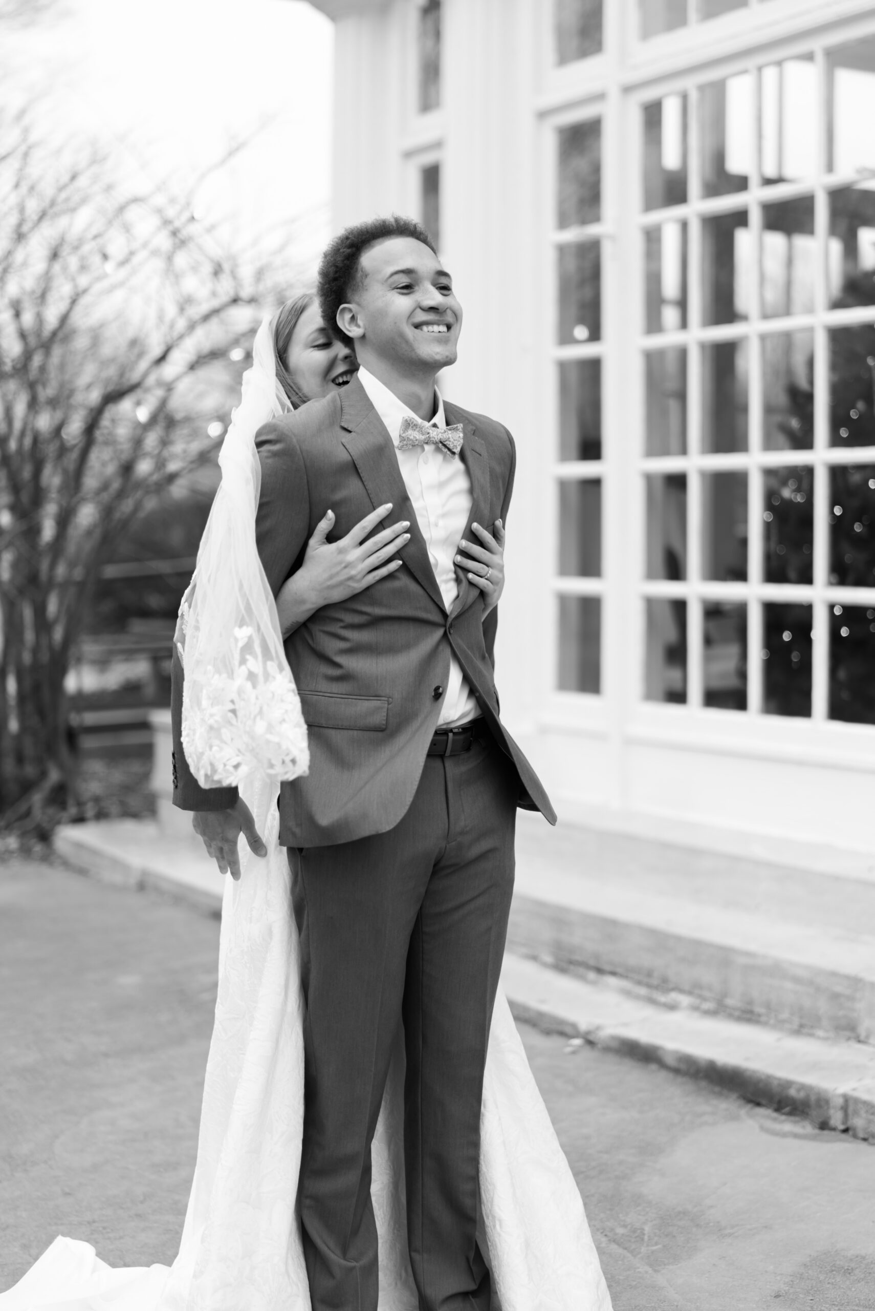 Black and white photo of bride hugging groom from behind during wedding portraits